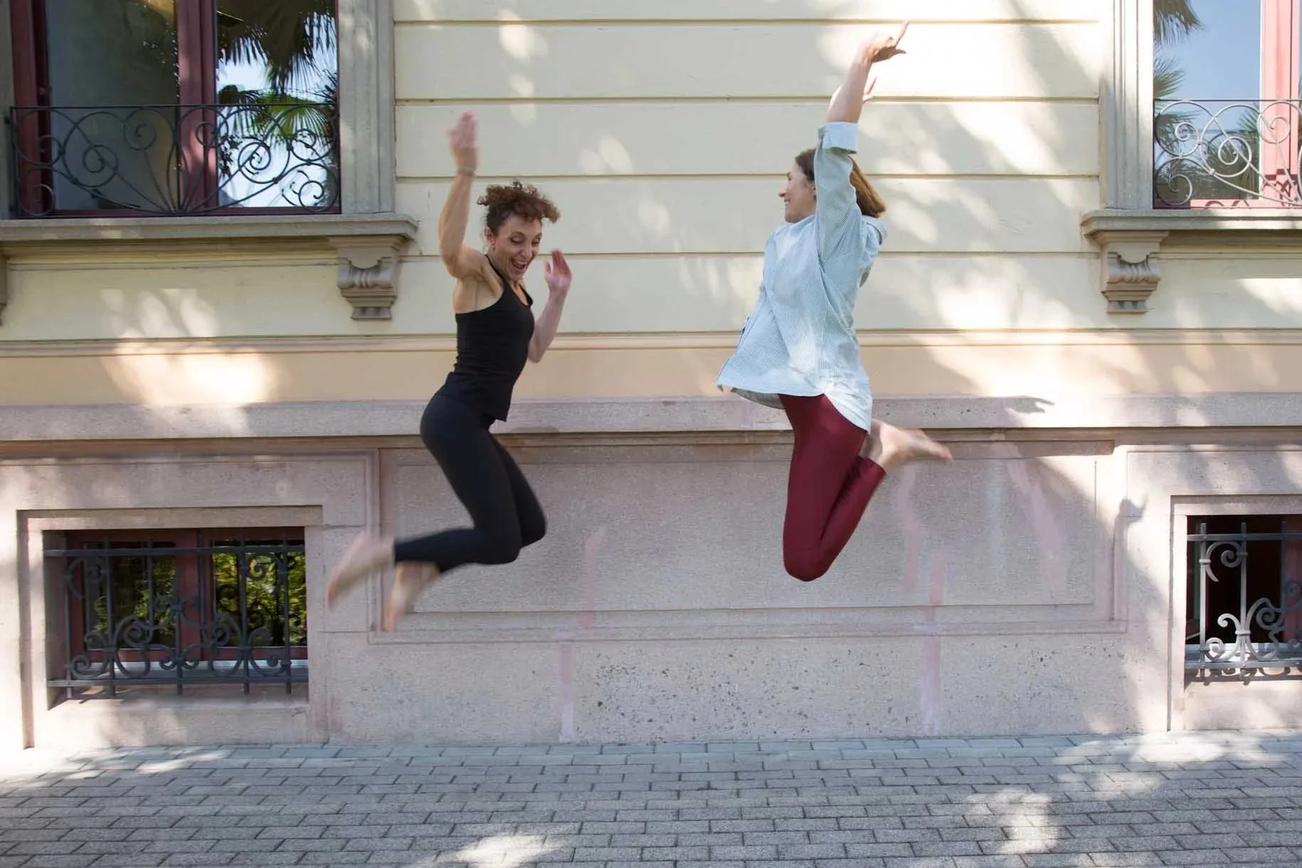 Two women joyfully jumping outdoors in front of a building