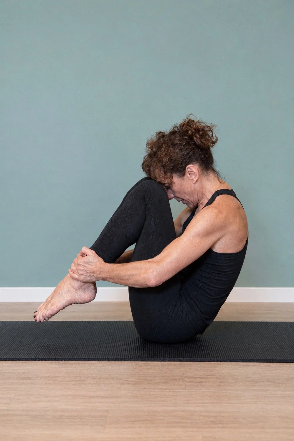 Phaedra Imbert balances in the starting position on the mat for Pilates Rolling Like a Ball, holding her bent legs close to her chest.