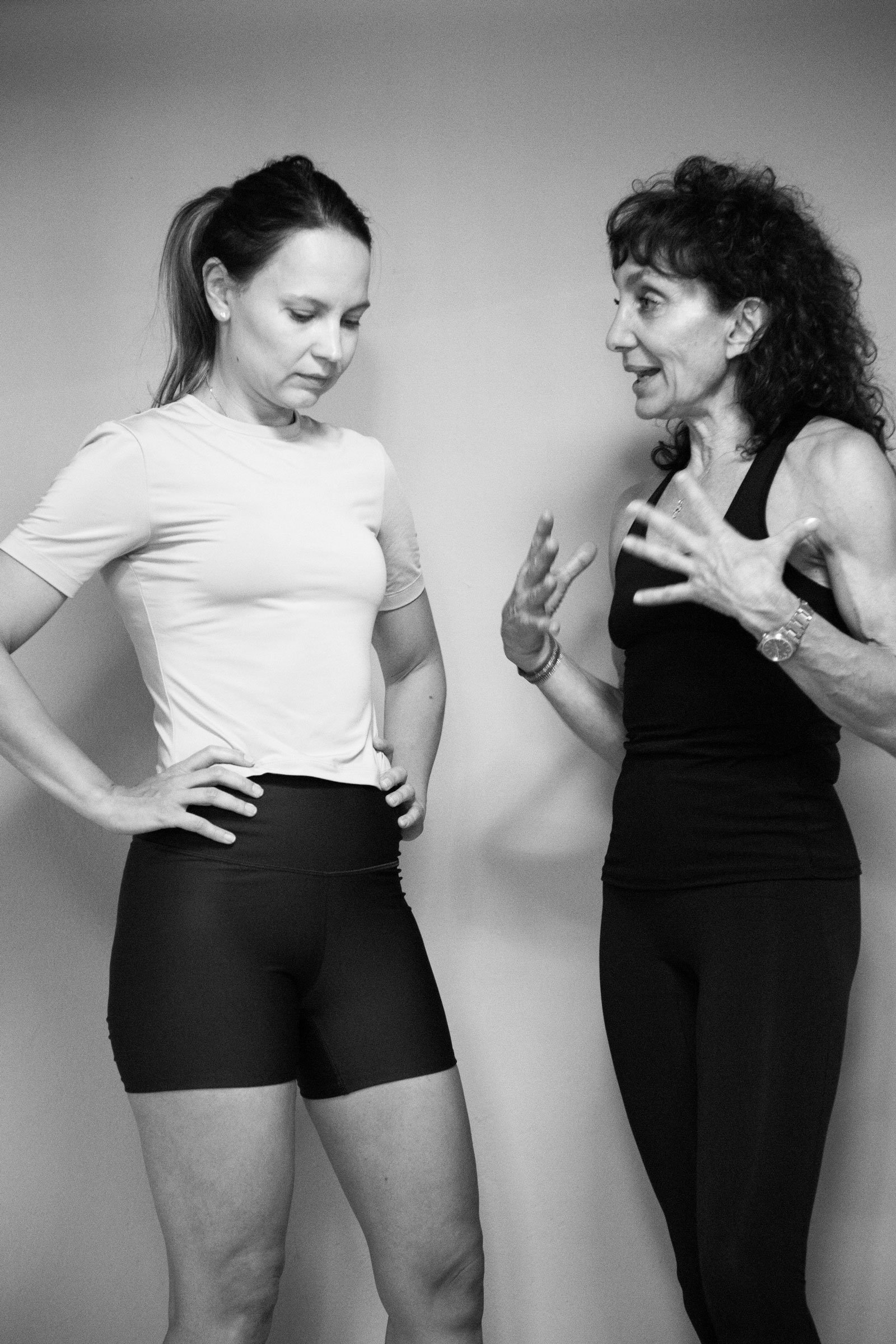 Black-and-white photo of two women conversing, with one gesturing and the other standing with her hands on her hips.