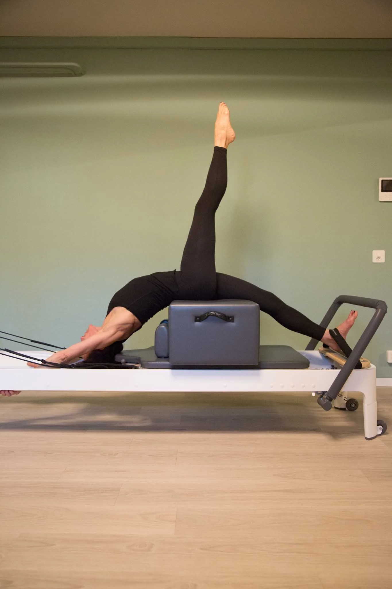 Person performing a split-leg Pilates exercise on a reformer machine.