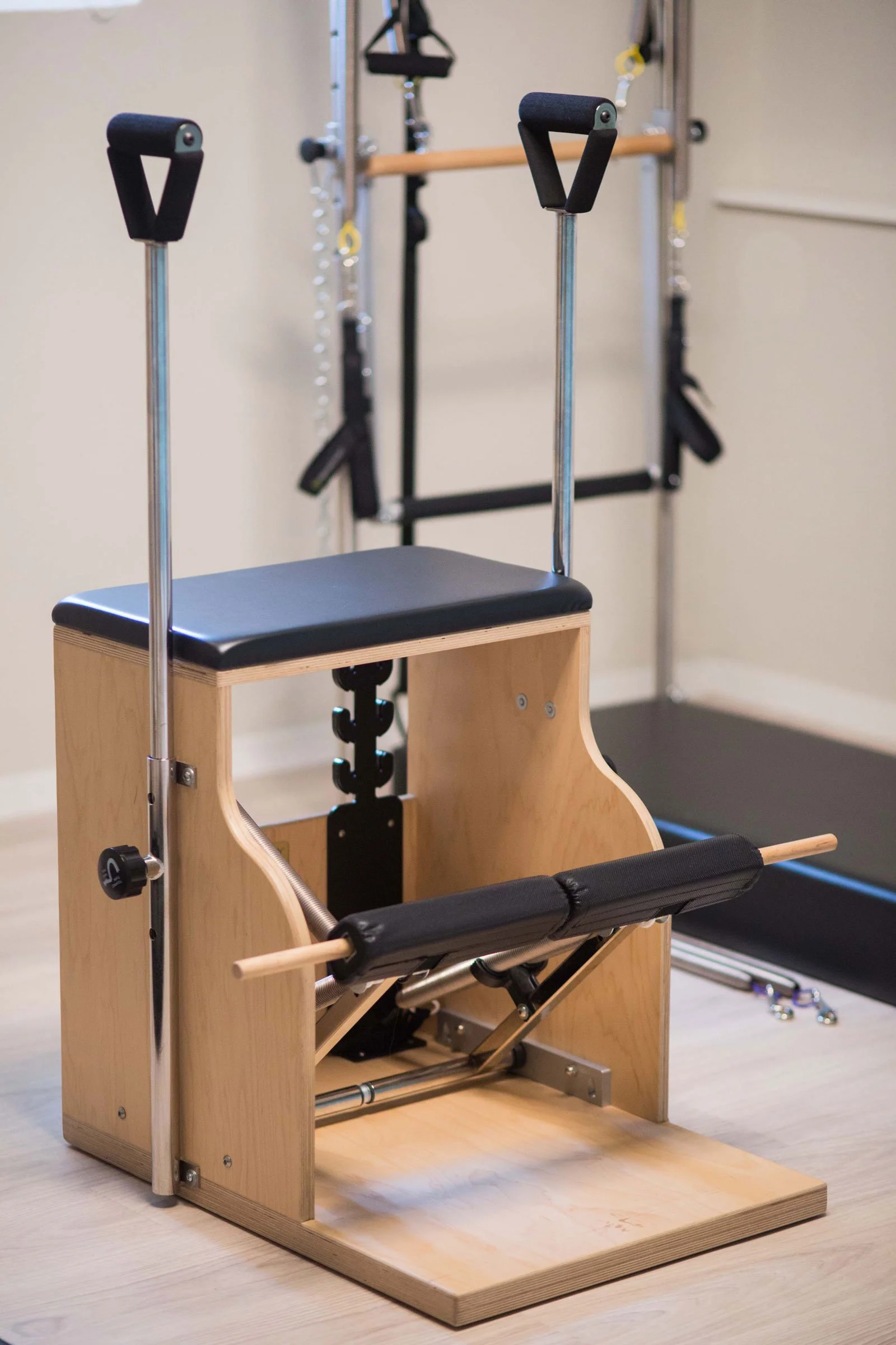 Wooden Pilates ladder barrel exercise apparatus with padded seat, handles, springs, and rolling bar in a fitness studio