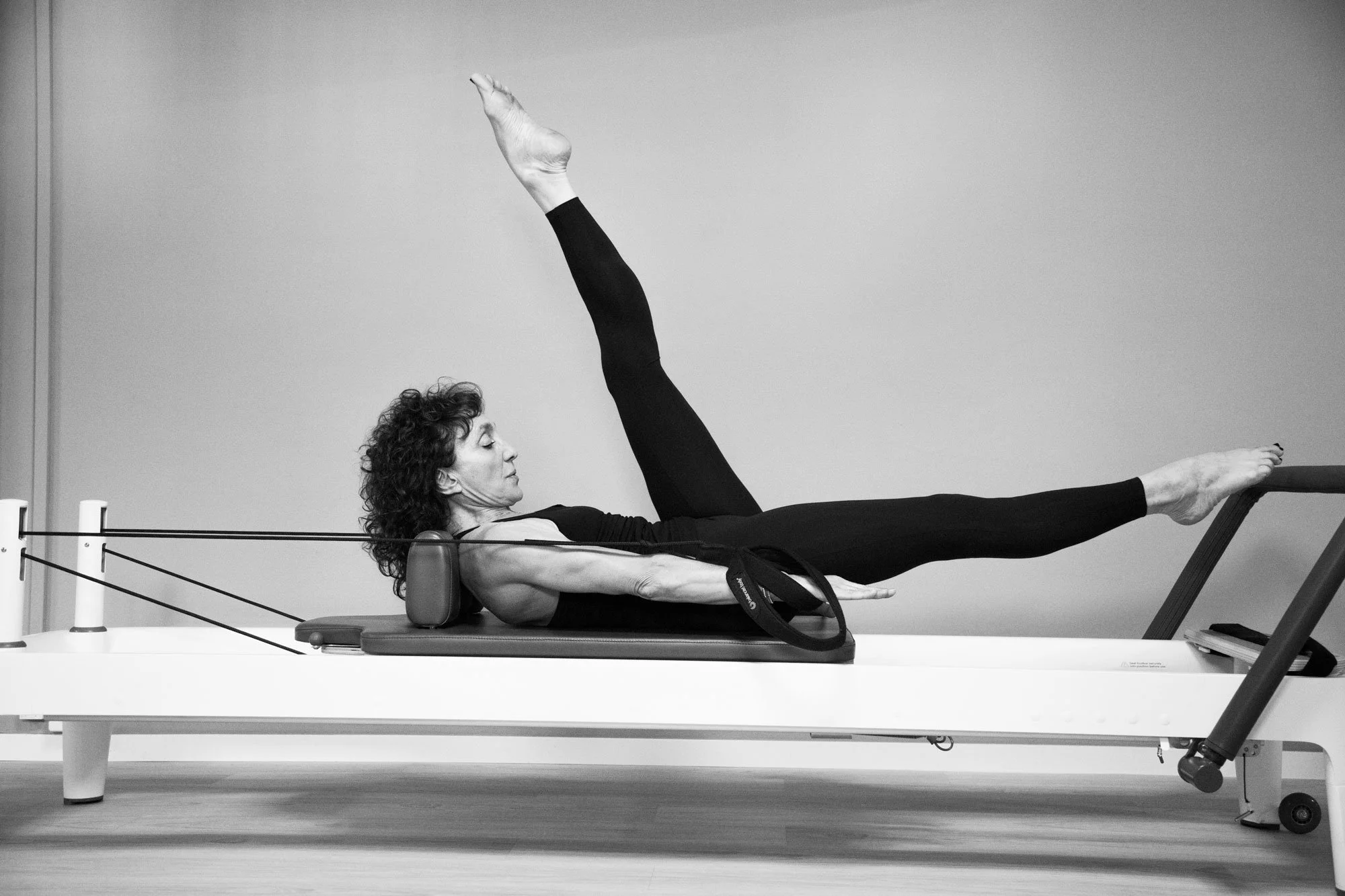 Pilates Reformer Scissors: Phaedra Imbert lies on the carriage with one leg lifted and the other extended away.