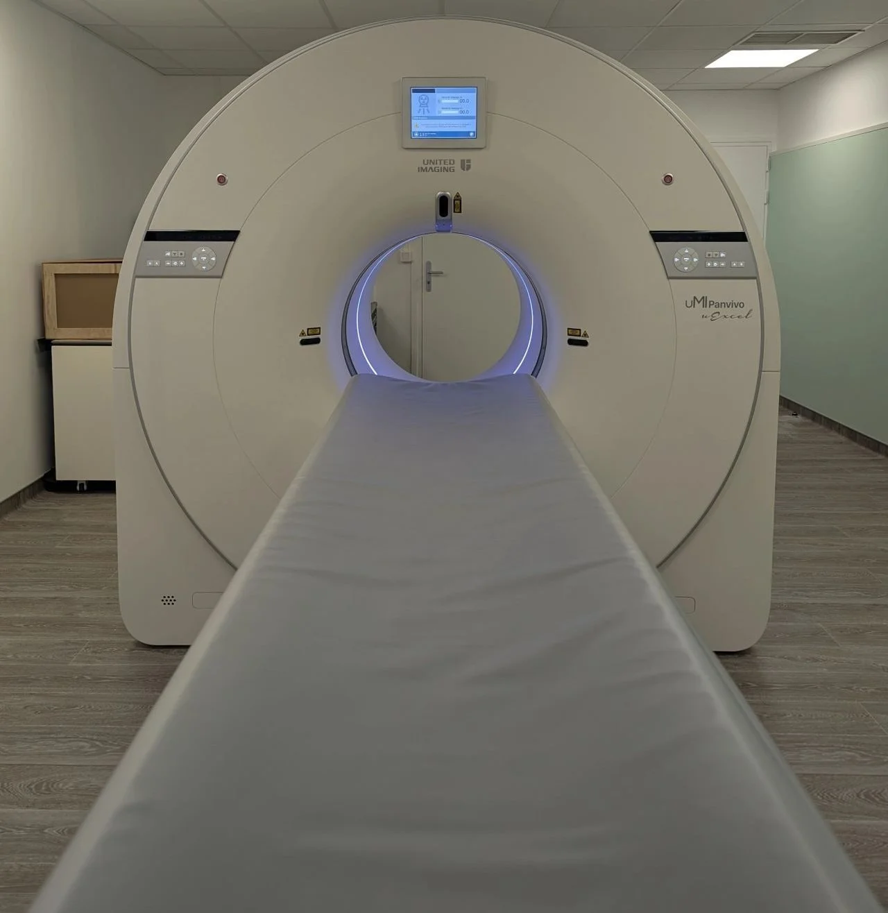A medical United Imaging CT scanner in a hospital room, with a patient table extending into the machine's circular opening.