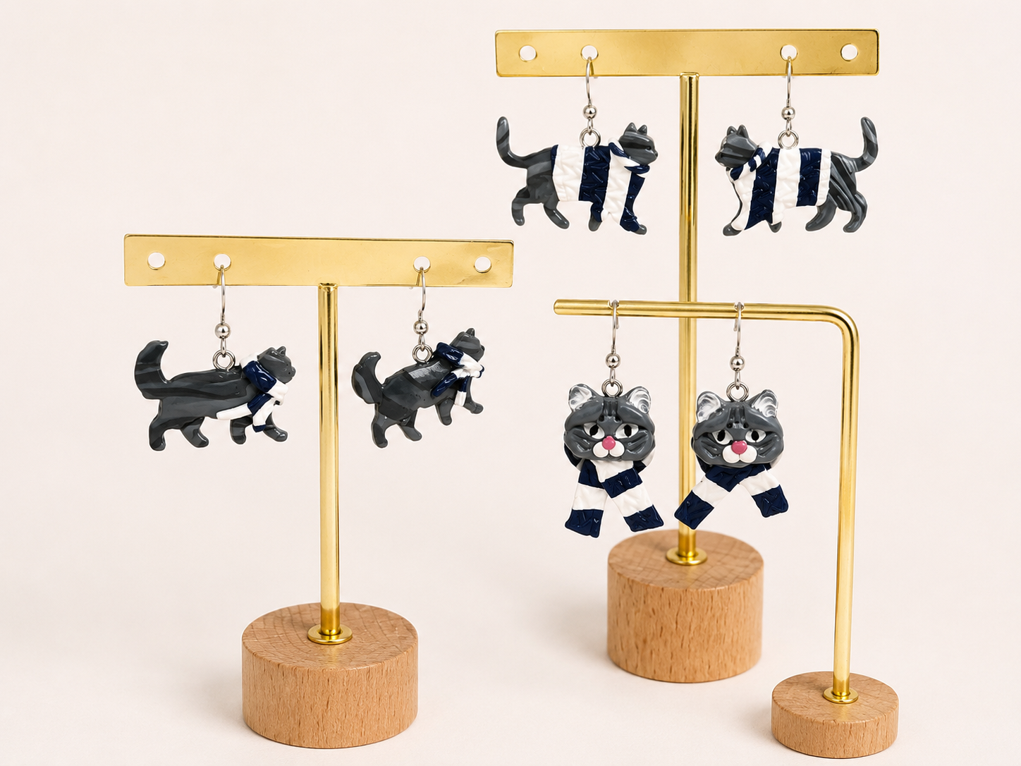 Two gold jewelry display stands with black cat-shaped earrings and black cat-shaped dangle charms dressed in white and navy stripes, set against a plain white background.