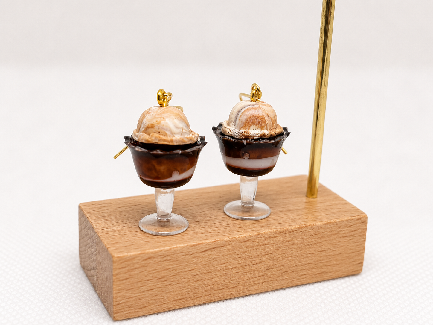 Two miniature dessert cups with chocolate and caramel ice cream, on a wooden block with a brass rod and white background.