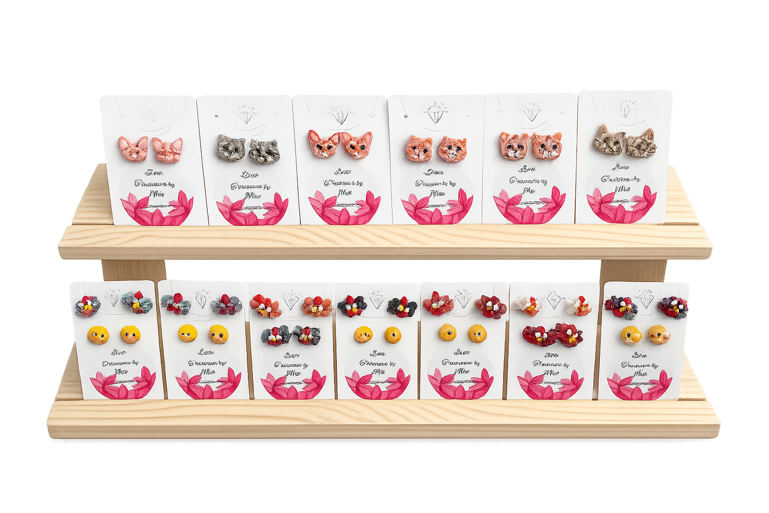 Display of various handmade jewelry pieces, including earrings and rings, on white cards with pink floral designs arranged on a wooden stand.