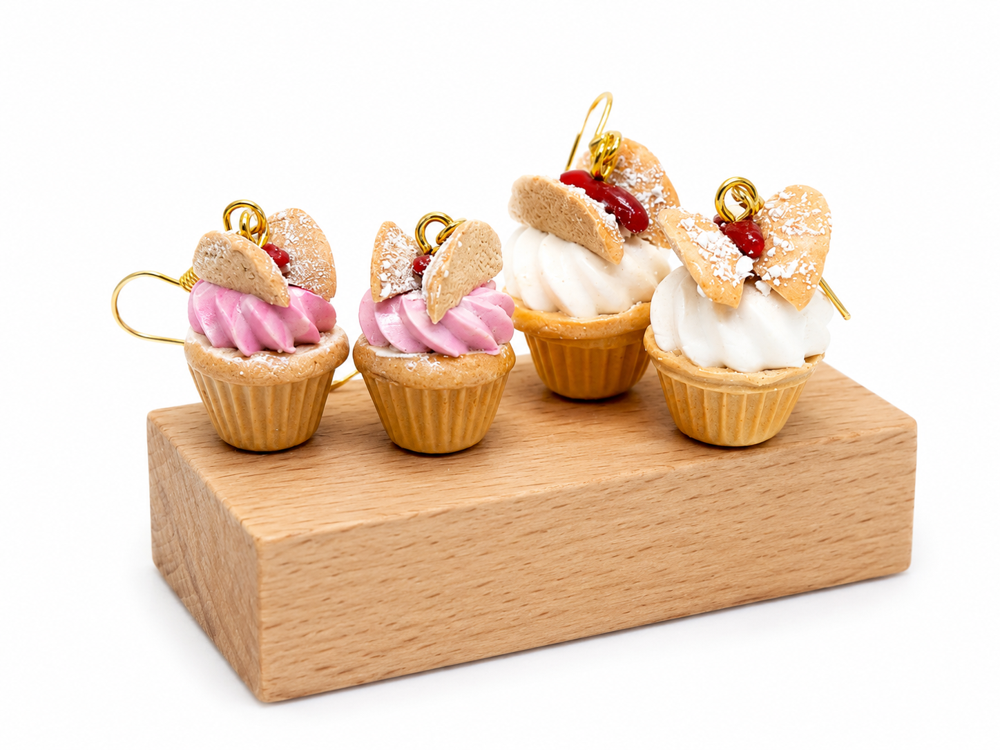 Four miniature cupcake charms with pink and white frosting, decorated with cookie slices and red cherry toppings, displayed on a wooden block.