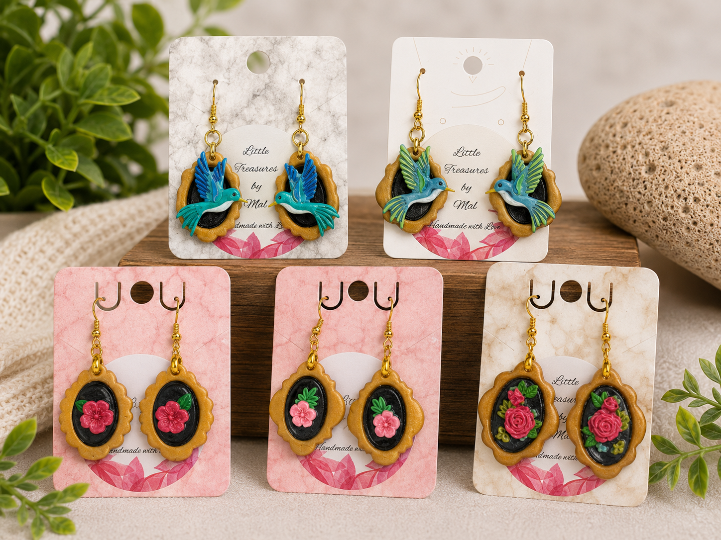 Six pairs of handmade earrings with floral and bird designs, displayed on colorful cards with 'joy' and 'little treasures' text, surrounded by plants and natural elements.