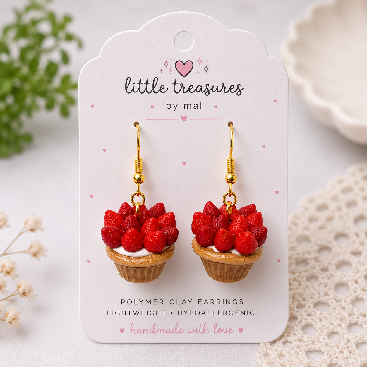 Earrings designed to look like mini strawberry cupcakes with red strawberries on top, attached to gold hooks, displayed on a white card that reads 'little treasures by mal' and 'polymer clay earrings, lightweight, hypoallergenic, handmade with love'.