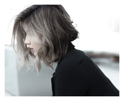 Side profile of a woman with shoulder-length, wavy hair and light highlights, wearing a black top, in an indoor setting.