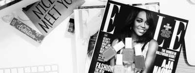 A magazine featuring a woman on the cover surrounded by nail polish bottles, placed on a cluttered desk with other papers and a keyboard.