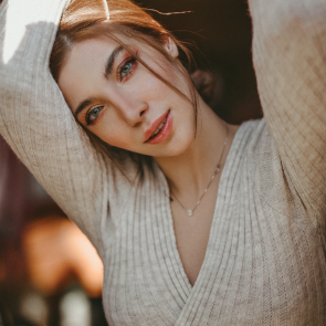 A young woman with light brown hair and blue eyes, wearing a beige sweater, looking at the camera with a slight smile.