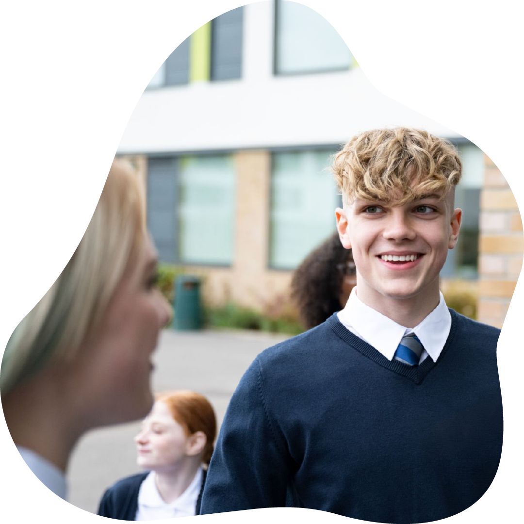 Smiling male school student with curly blonde hair in a school uniform standing outside of school.