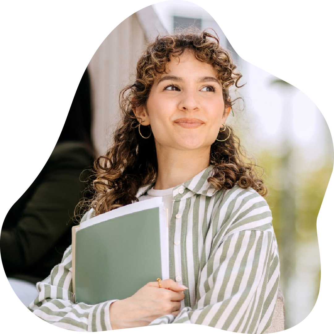 Young female student with curly hair and hoop earrings holding a green notebook, outdoors with a school building in the background.