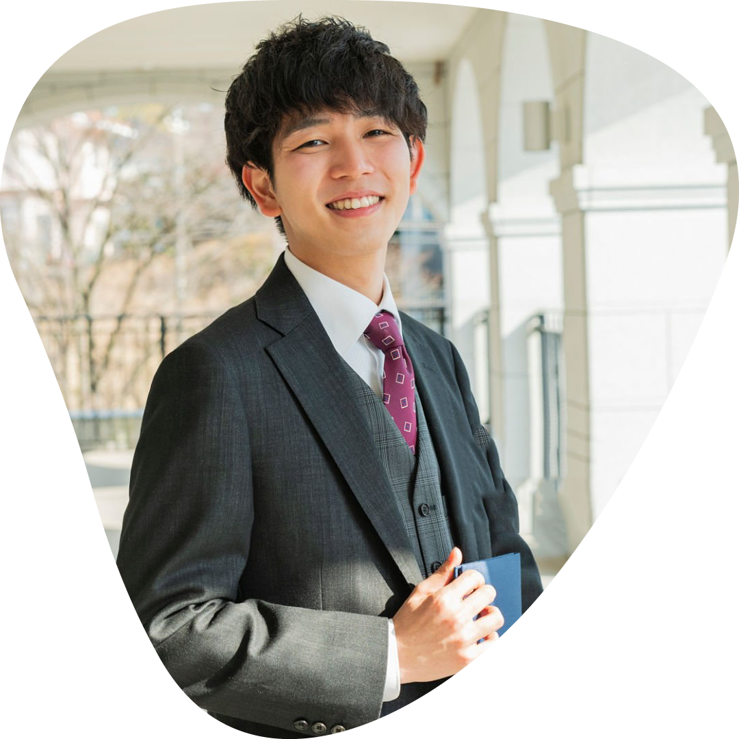 A young male student in school uniform and tie holding a school book and smiling outdoors.