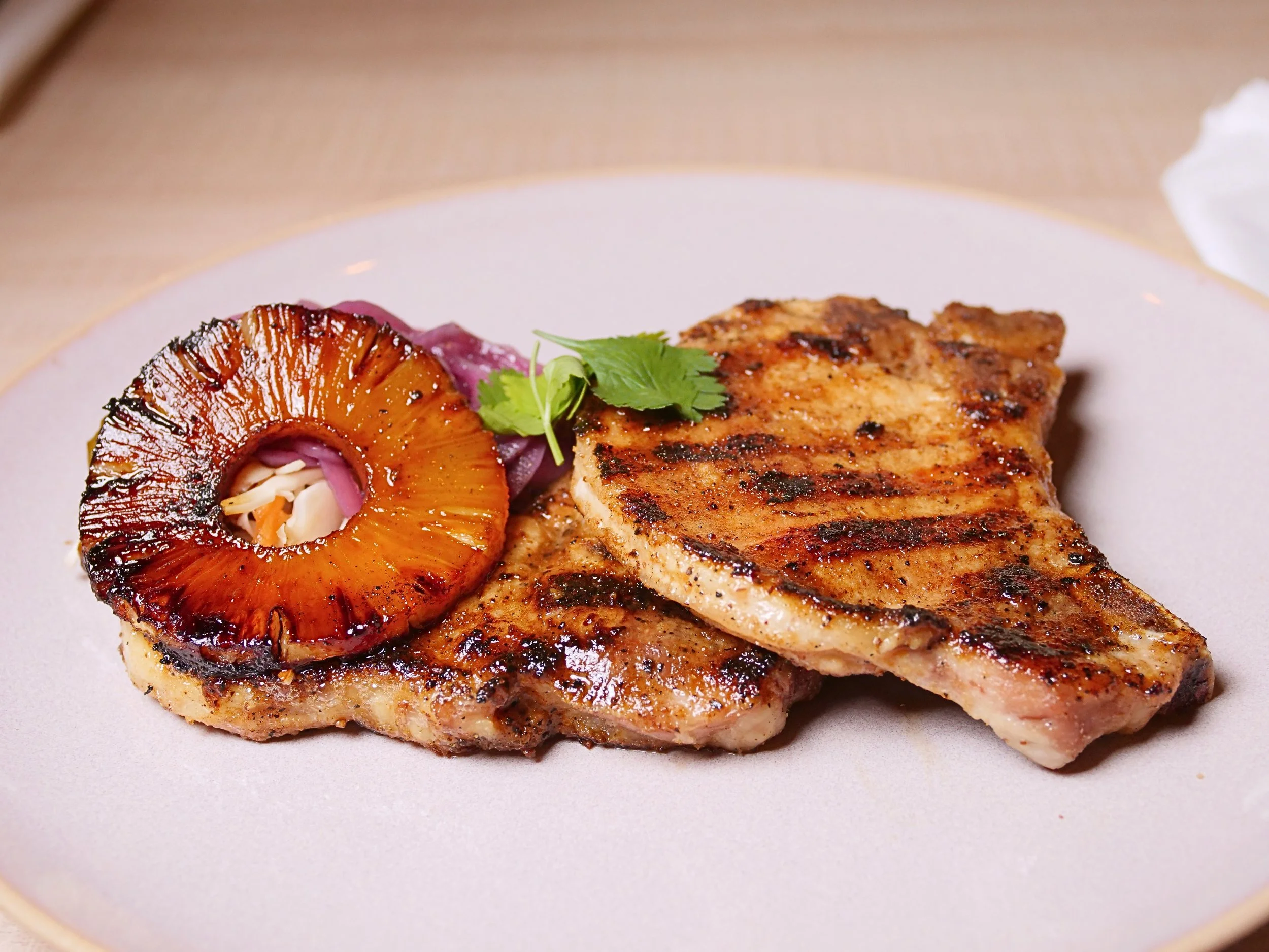 Close-up of grilled chicken breast topped with a pineapple slice and garnished with cilantro, served on a white plate.