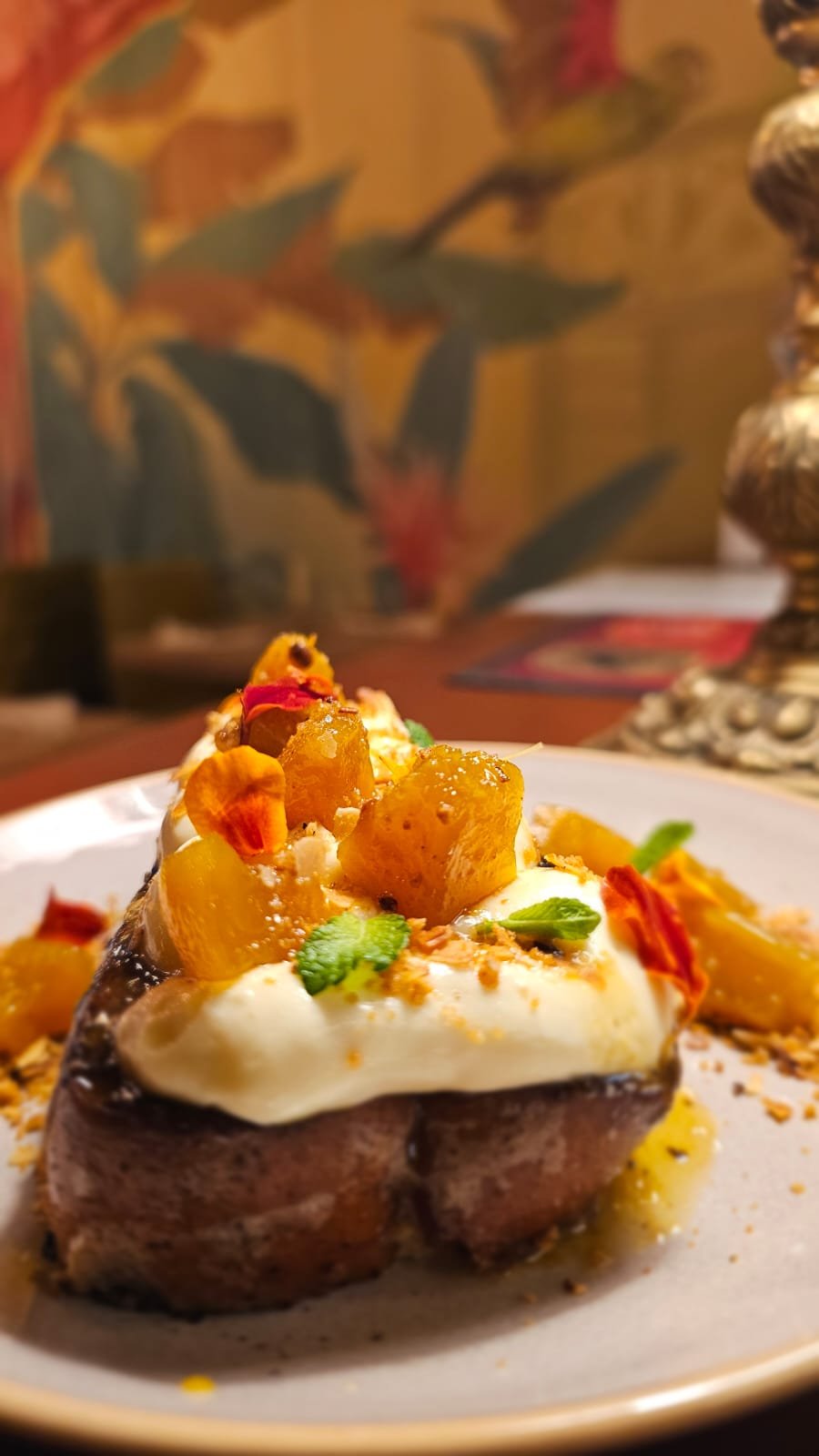 A plated breakfast dish features a slice of toasted bread topped with a fried egg, pineapple chunks, and garnished with small vegetables and crumbled toppings.
