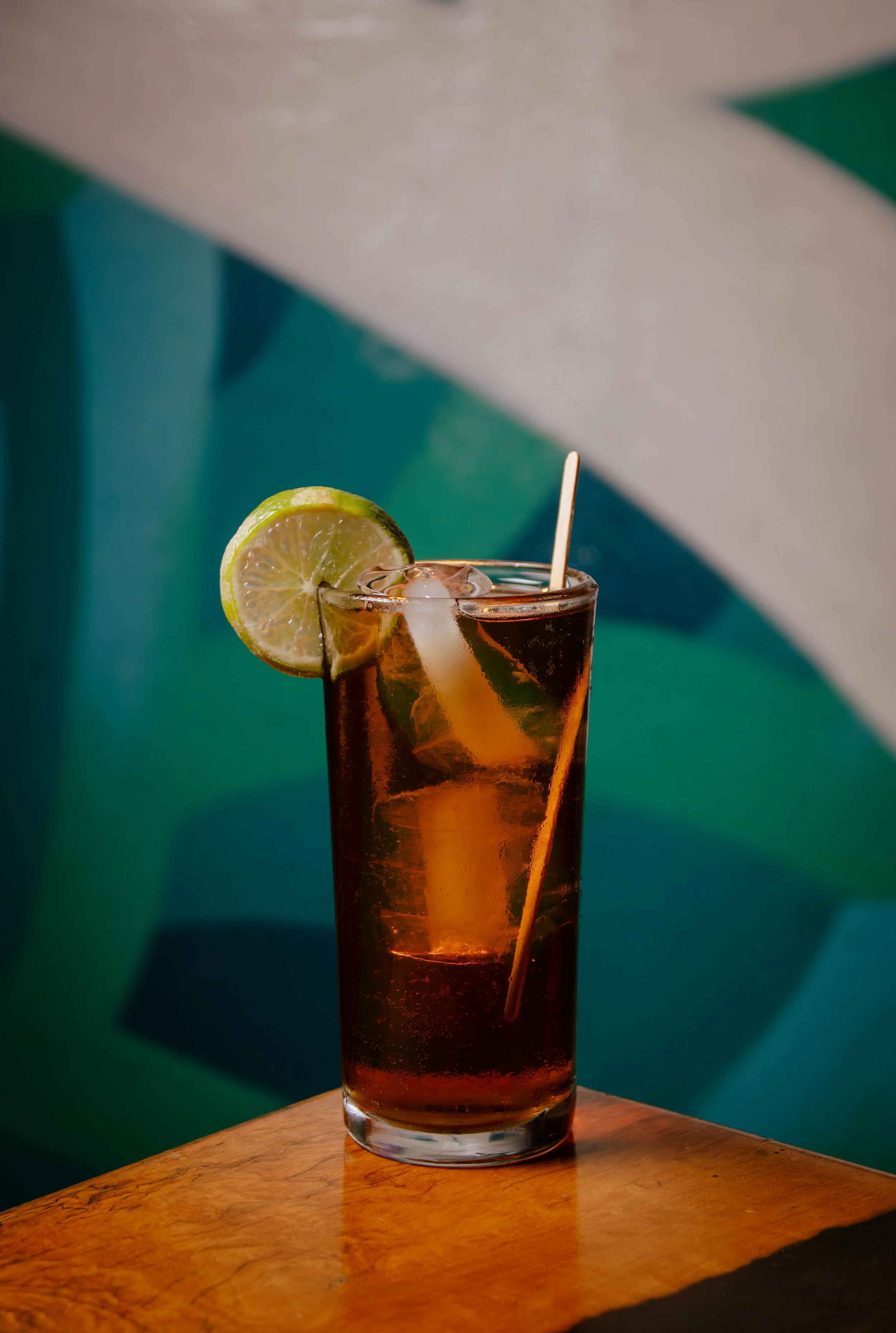 A tall glass of iced tea with a lemon slice on the rim and a drinking straw, placed on a wooden surface with a colorful abstract background.