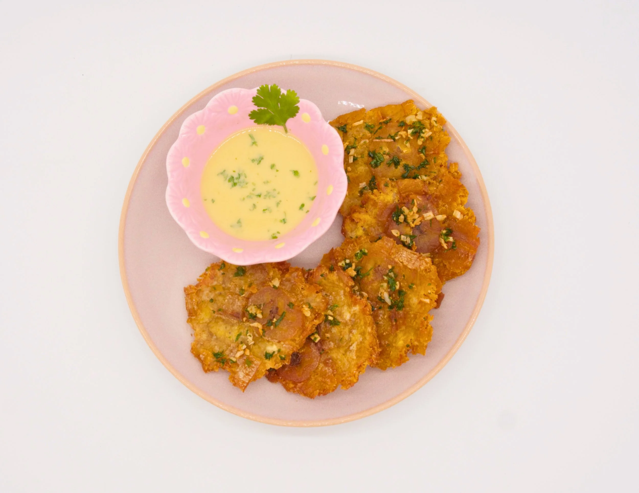 Fried food served with a dipping sauce, garnished with chopped herbs and a coriander leaf, on a pink plate with a small pink bowl