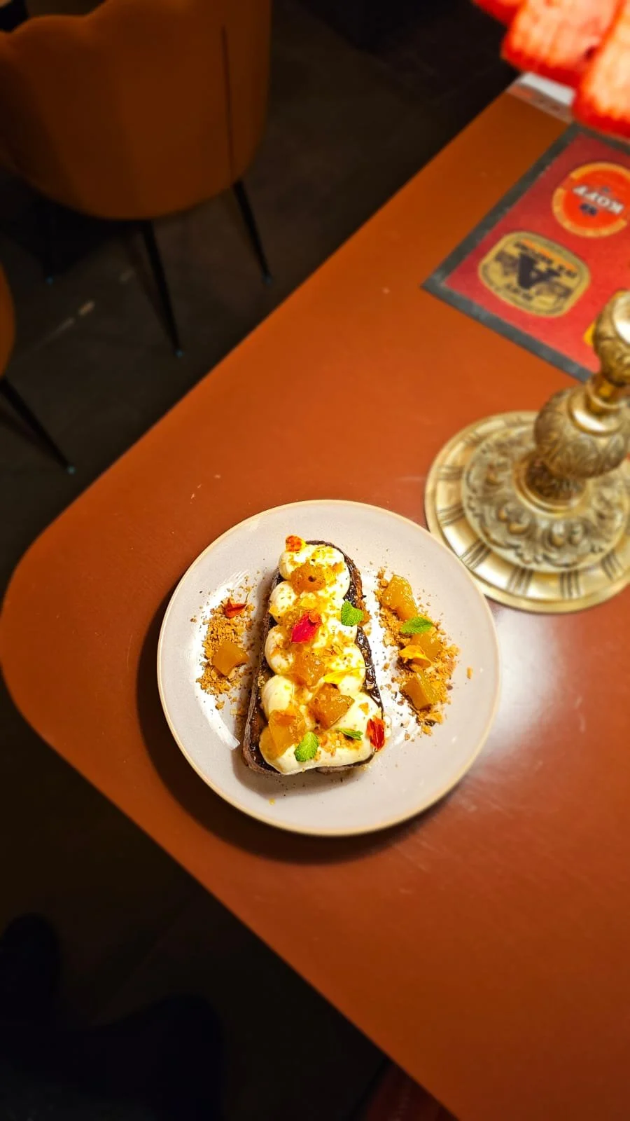 A dessert with cream, fruit, and garnish on a white plate, placed on a wooden table with a decorative candle holder nearby.