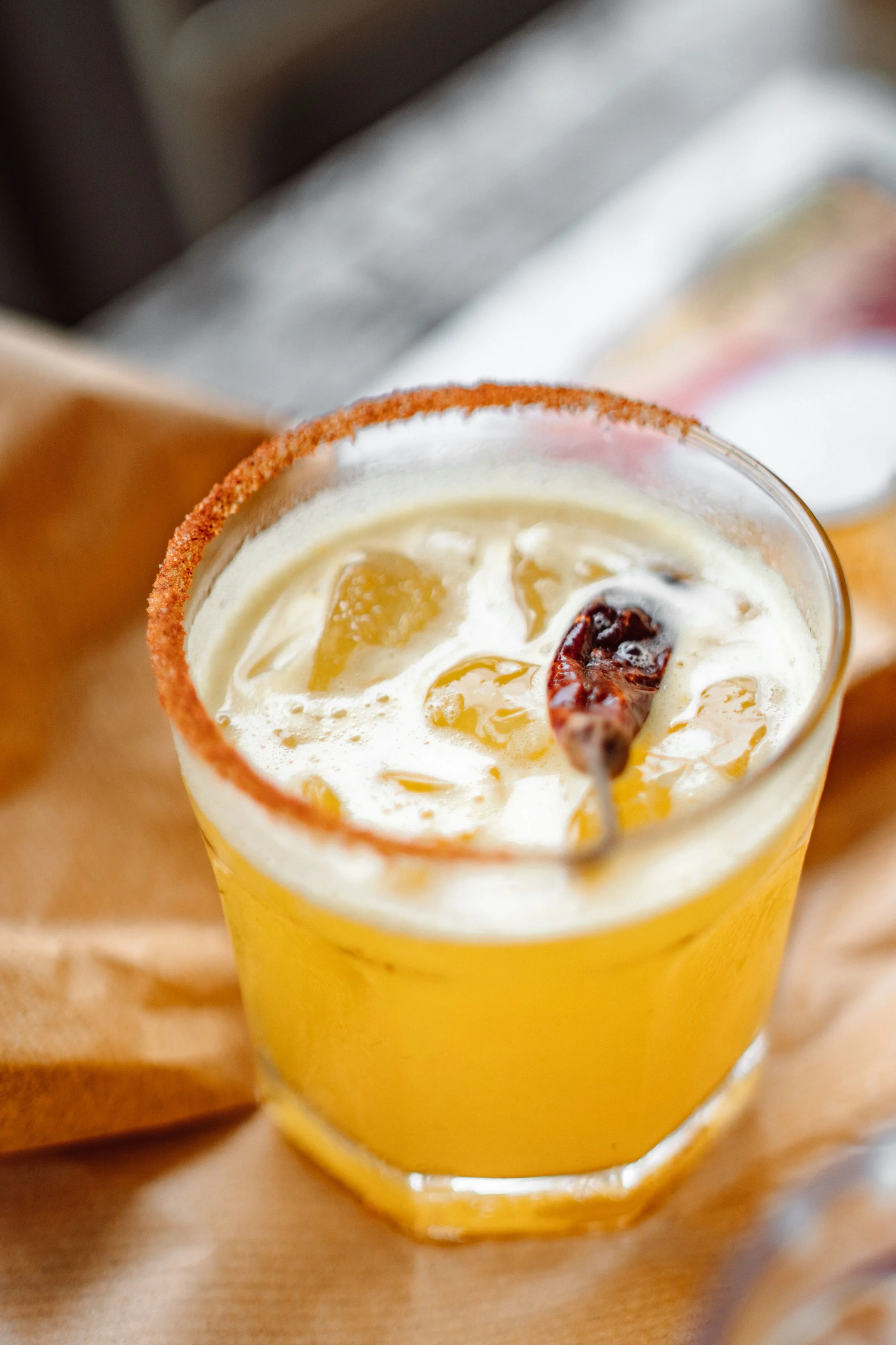 Close-up of a festive cocktail in a yellow glass, garnished with a sugar-rimmed edge, and topped with ice, dried fruit, and a cherry.