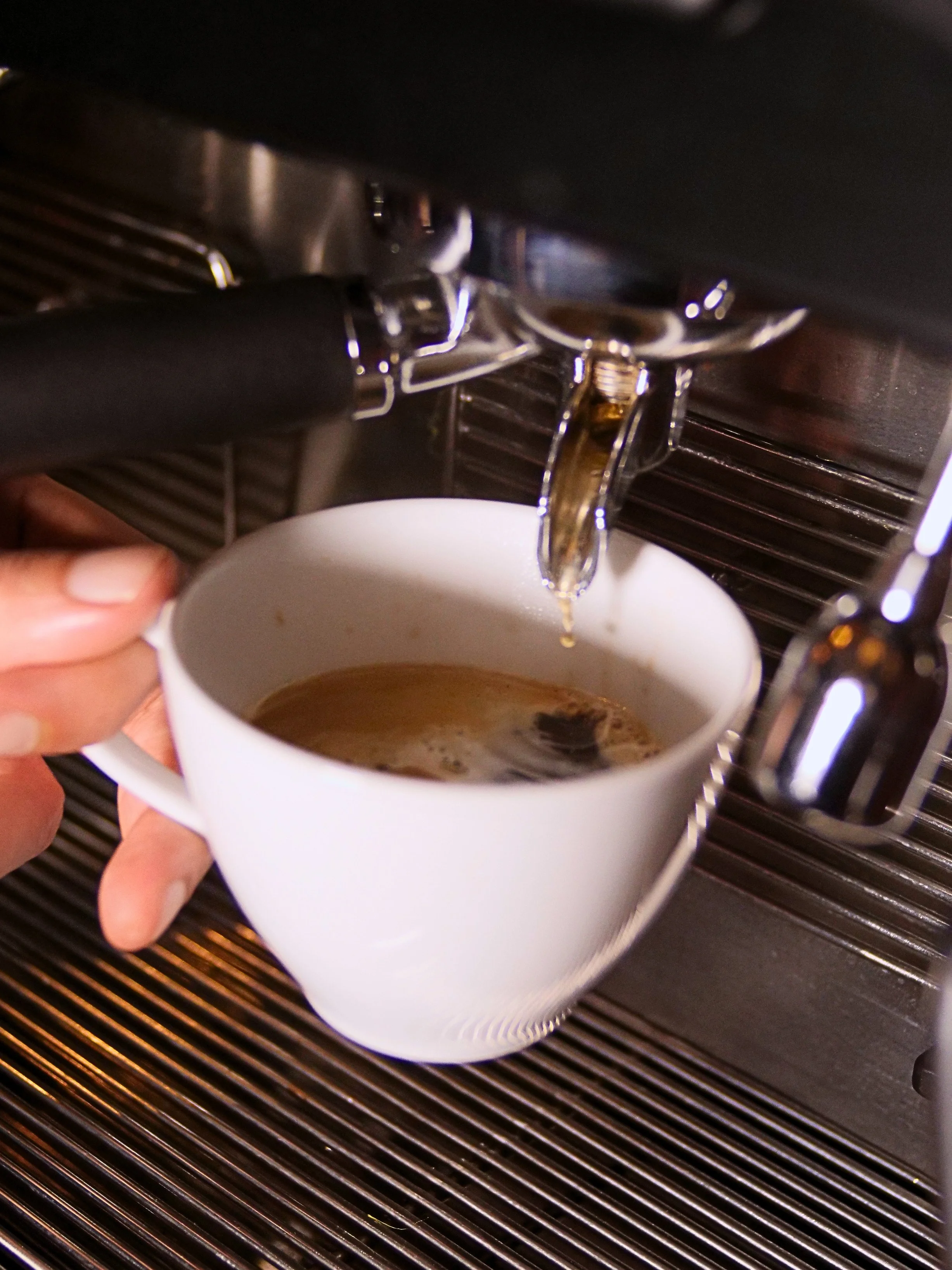 Close-up of a coffee machine pouring brewed coffee into a white mug, with a person's hand holding the mug.