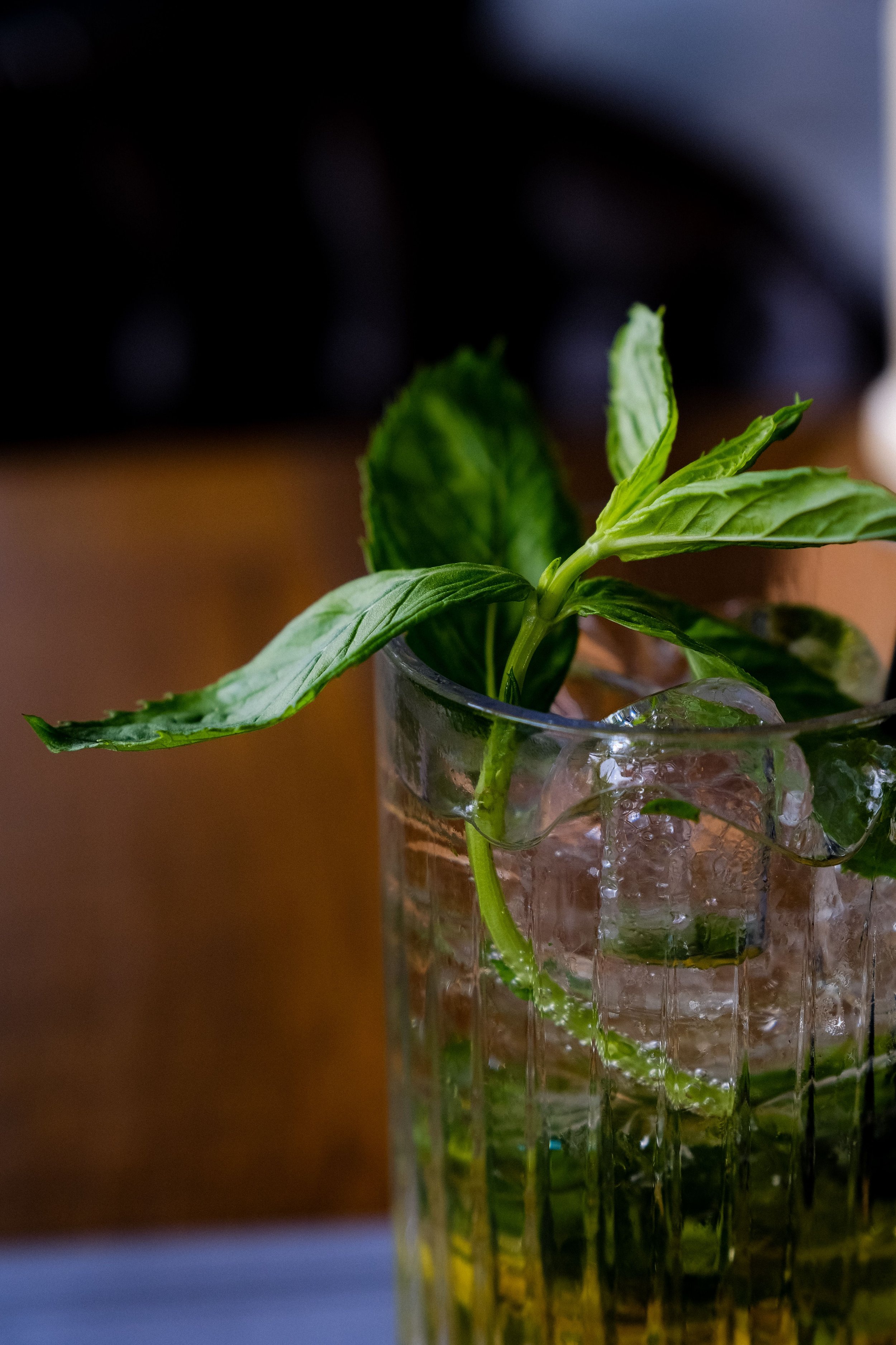 Close-up of fresh green mint leaves in a glass container filled with water, with a blurred dark background.
