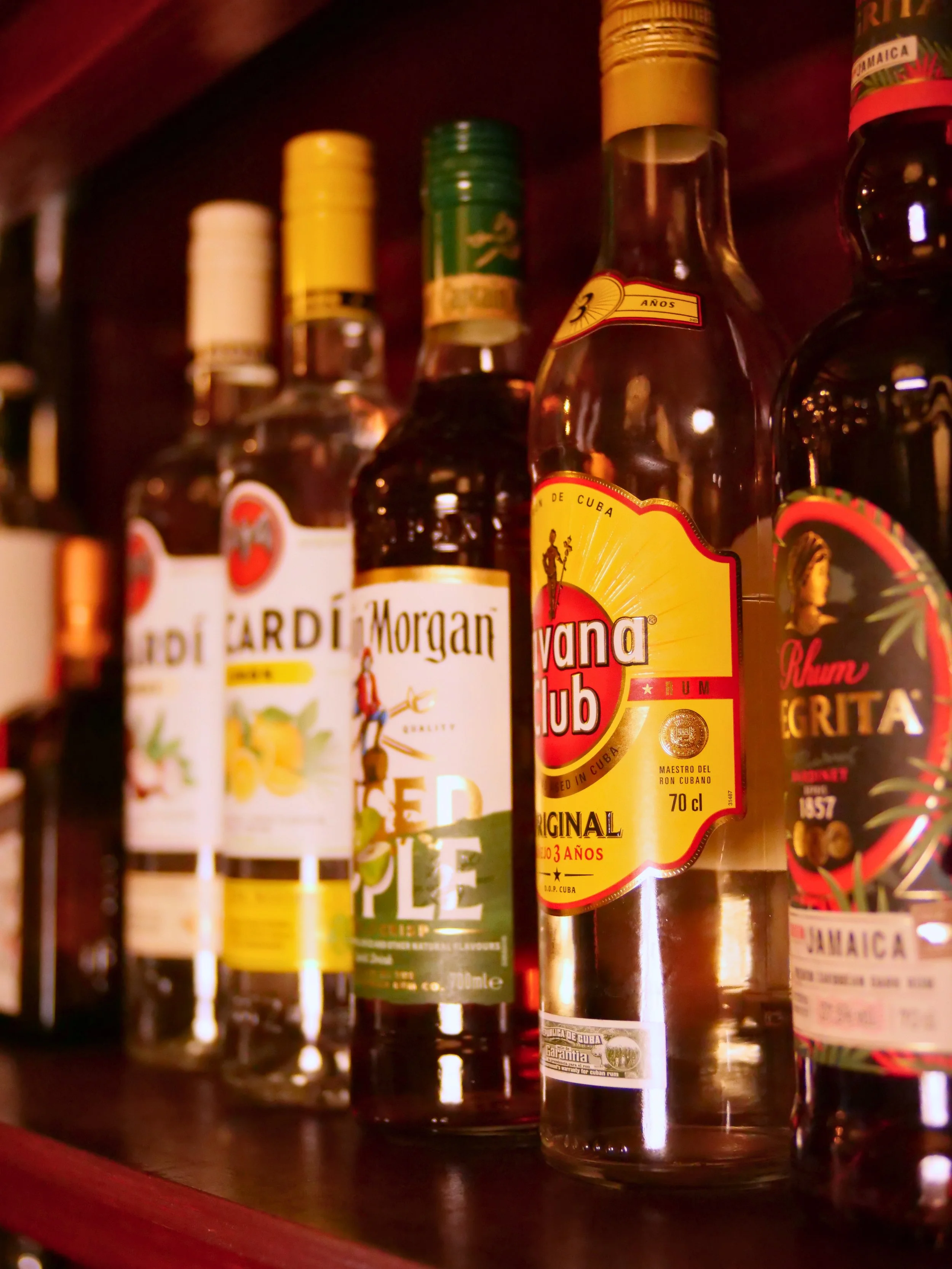 Various bottles of rum on a wooden shelf, including brands from Cuba, with labels and caps visible.