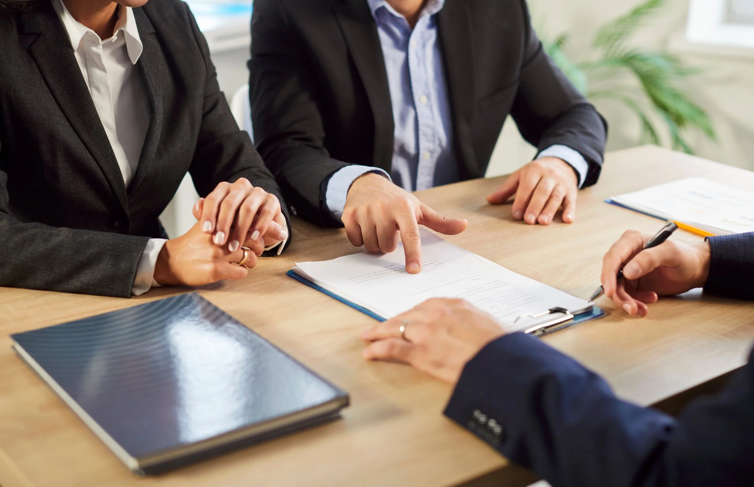 Two individuals in business attire discussing documents at a meeting table, with notebooks and papers on the table.