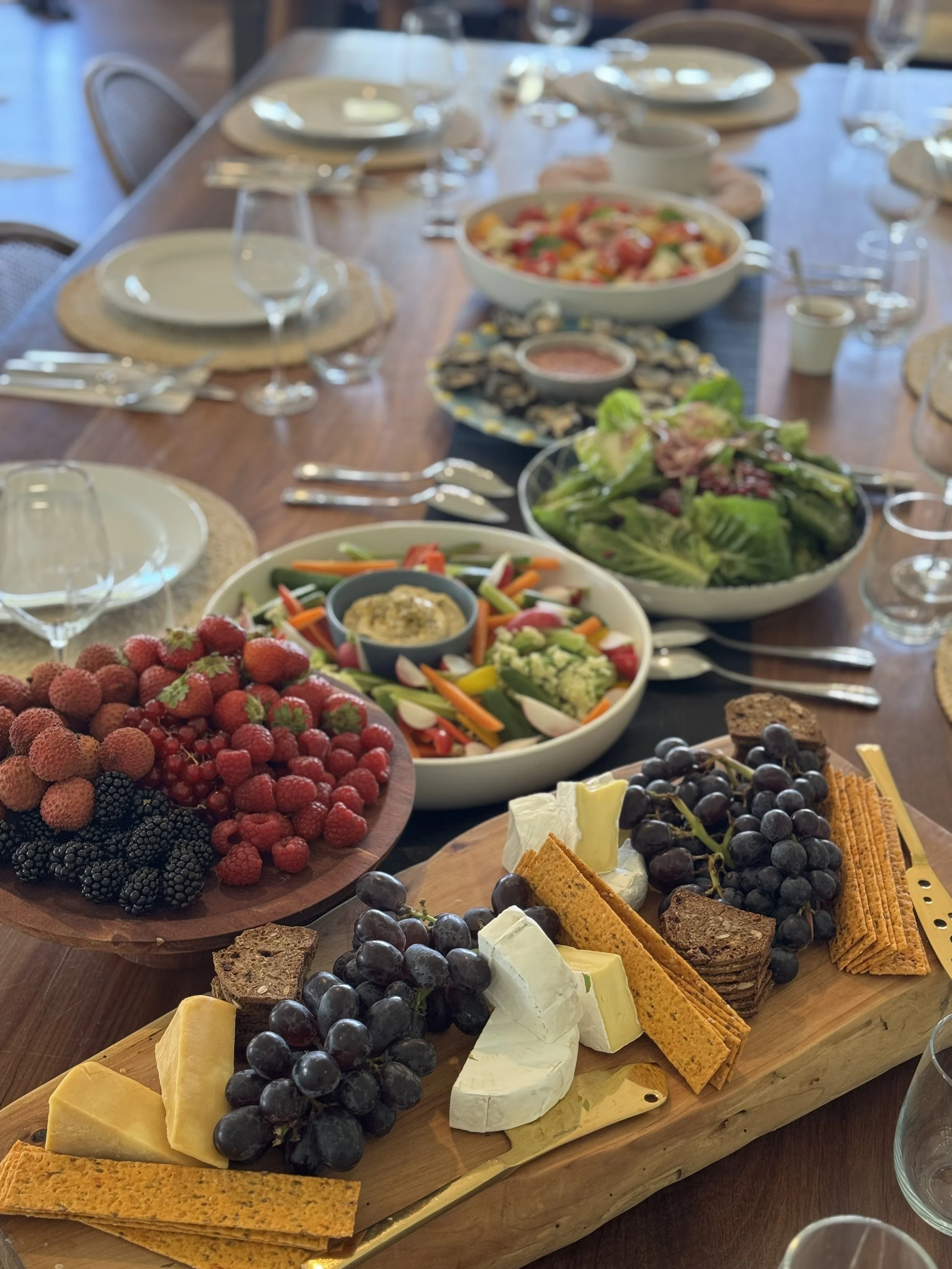 Assorted fresh fruits, cheeses, crackers, and vegetables arranged on wooden serving boards for a gathering.