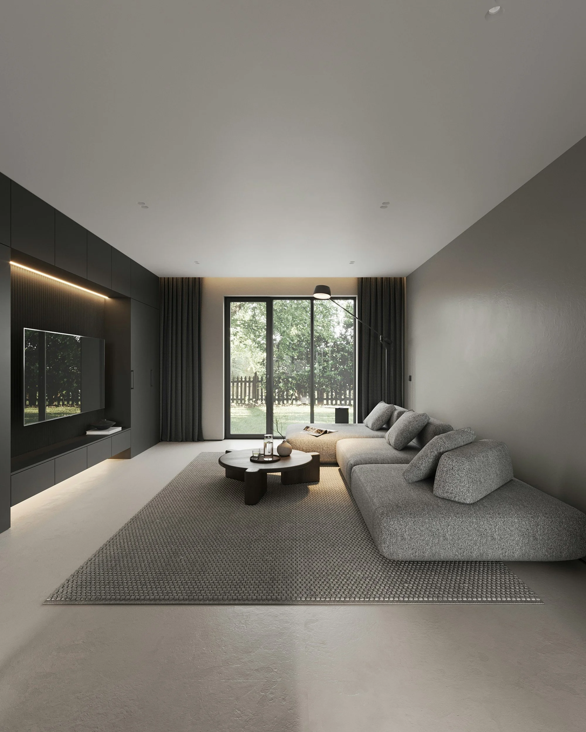 Living room with large window, gray sectional sofa, black round coffee table, textured rug, dark curtains, mounted TV, and minimal decor.