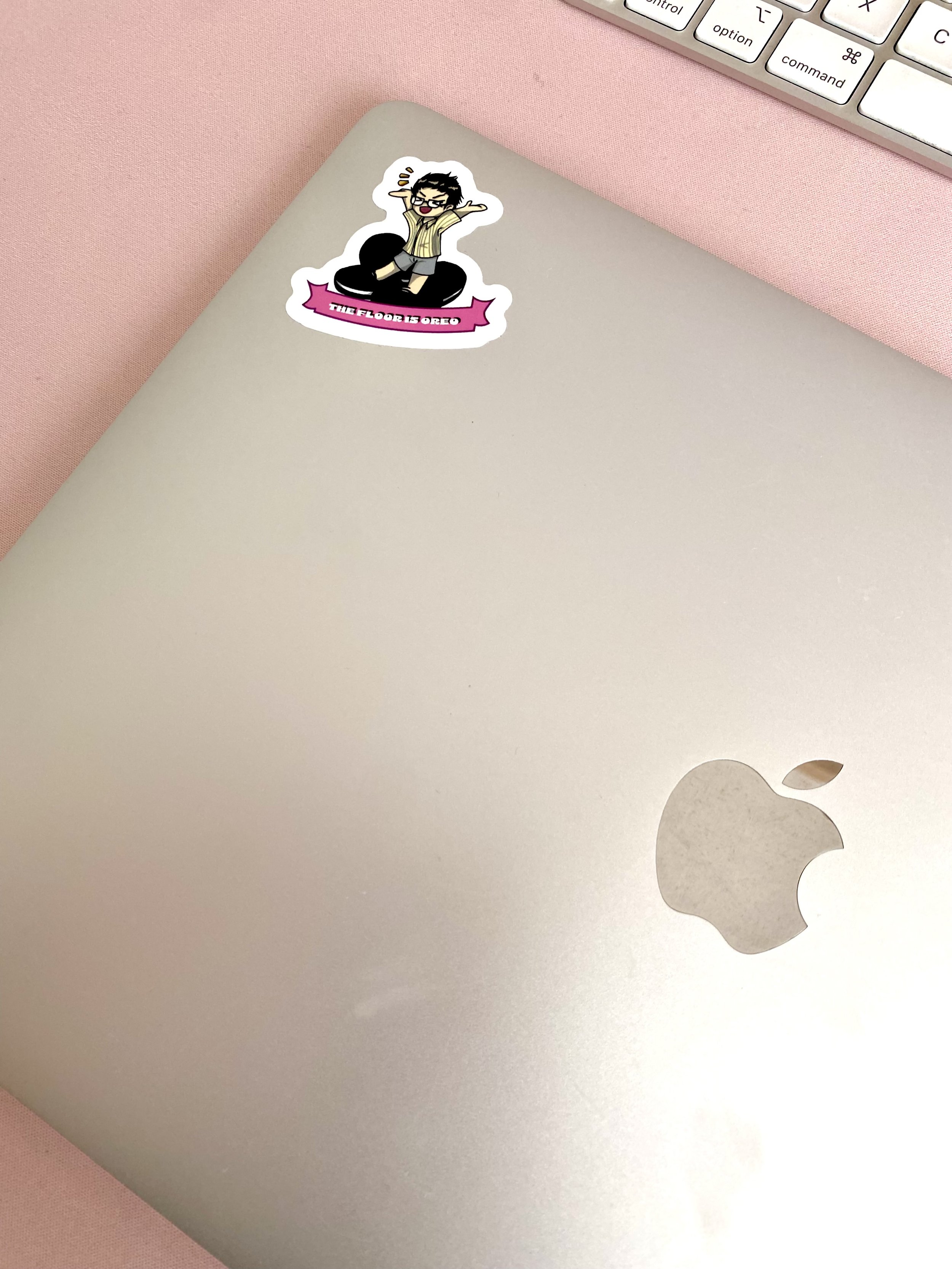 Silbernes Macbook mit Sticker liegt auf rosafarbener Unterlage.