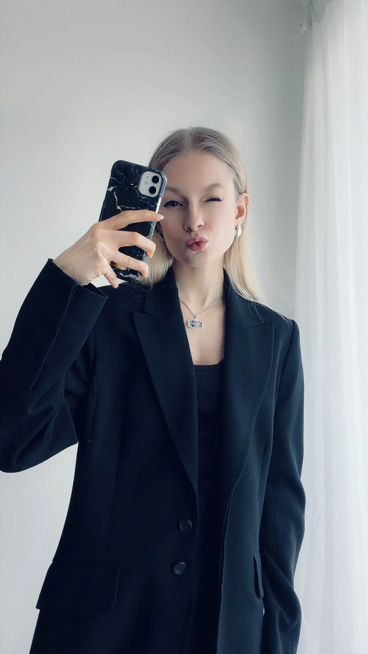 Blonde Frau mit schwarzem Anzug hält Handy in der Hand.