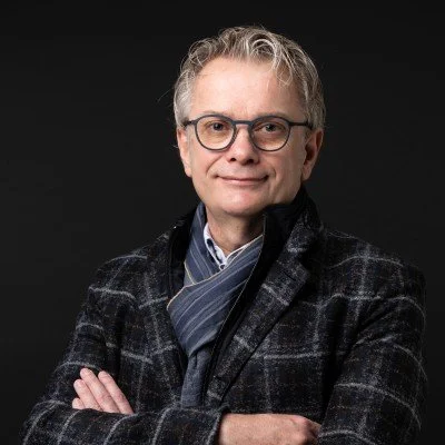 Mann mit Brille, grauen Haaren und kariertem Anzug lächelt zur Kamera.