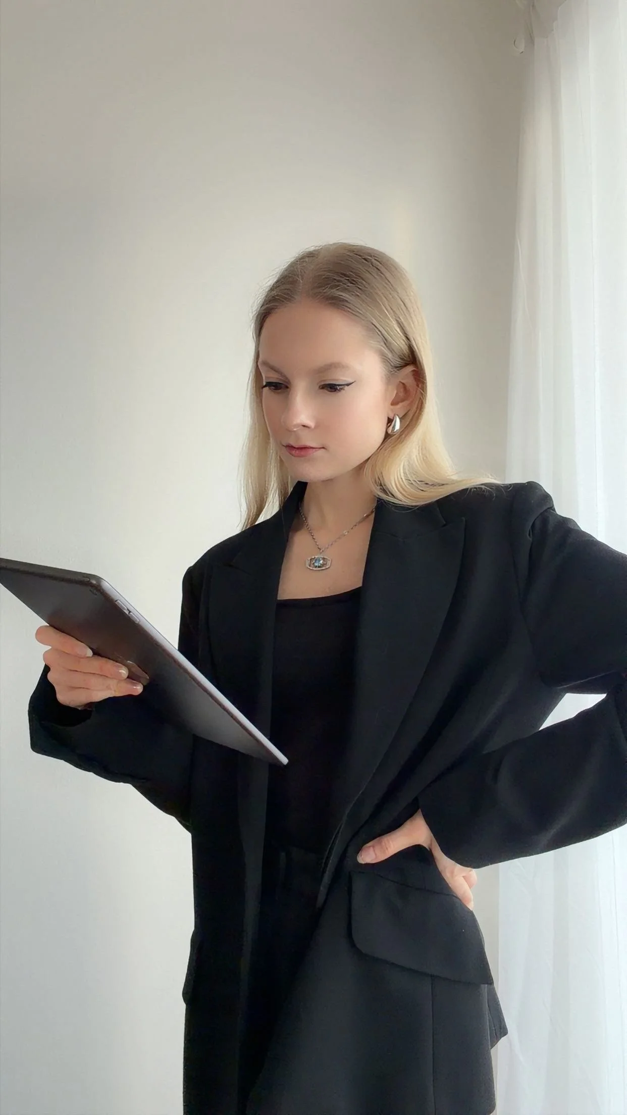 Blonde Frau mit schwarzem Hosenanzug blickt auf graues Tablet, welches sie in der Hand hält.