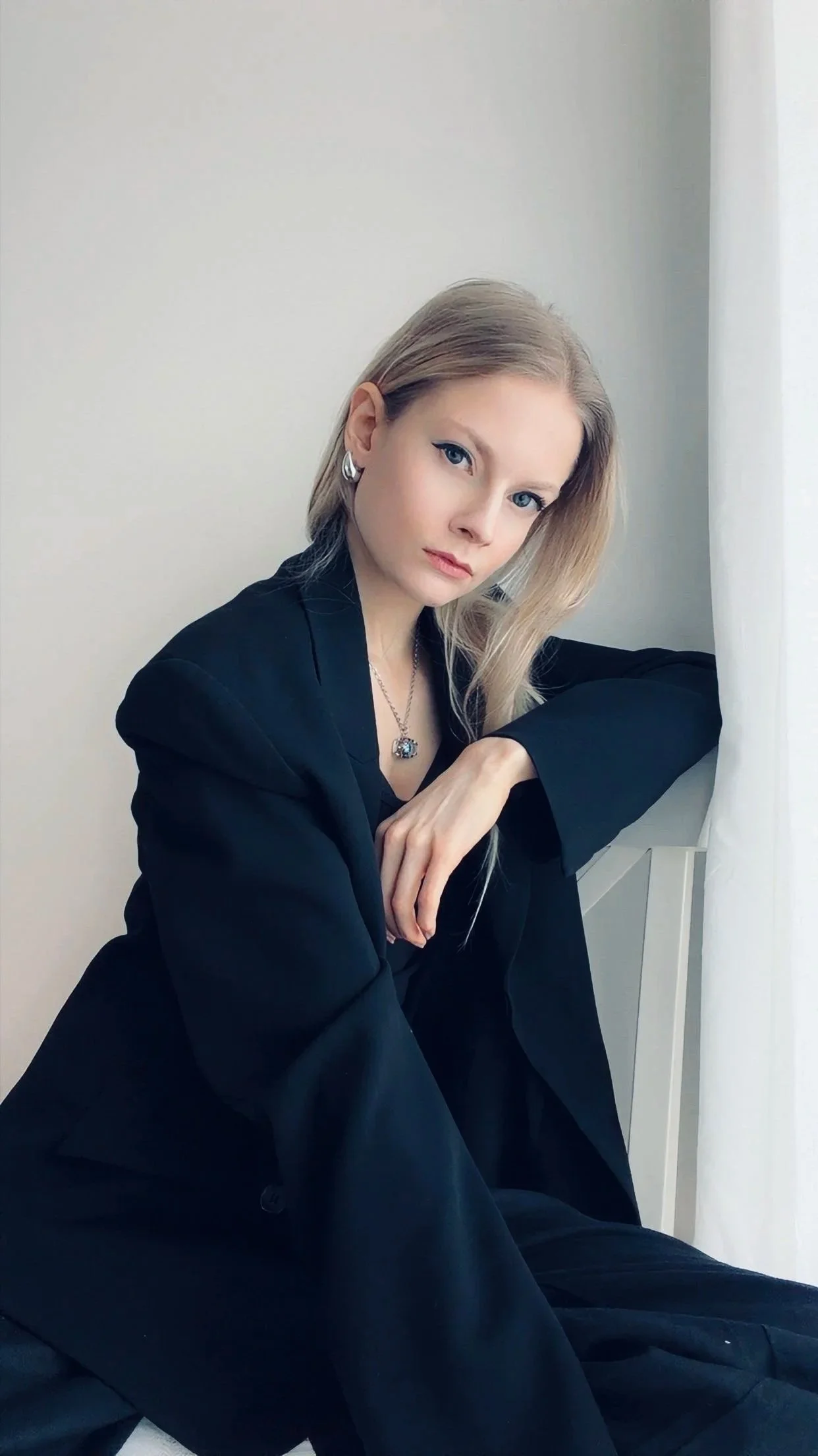 Blonde Frau mit blauen Augen und schwarzem Anzug blickt zur Kamera.