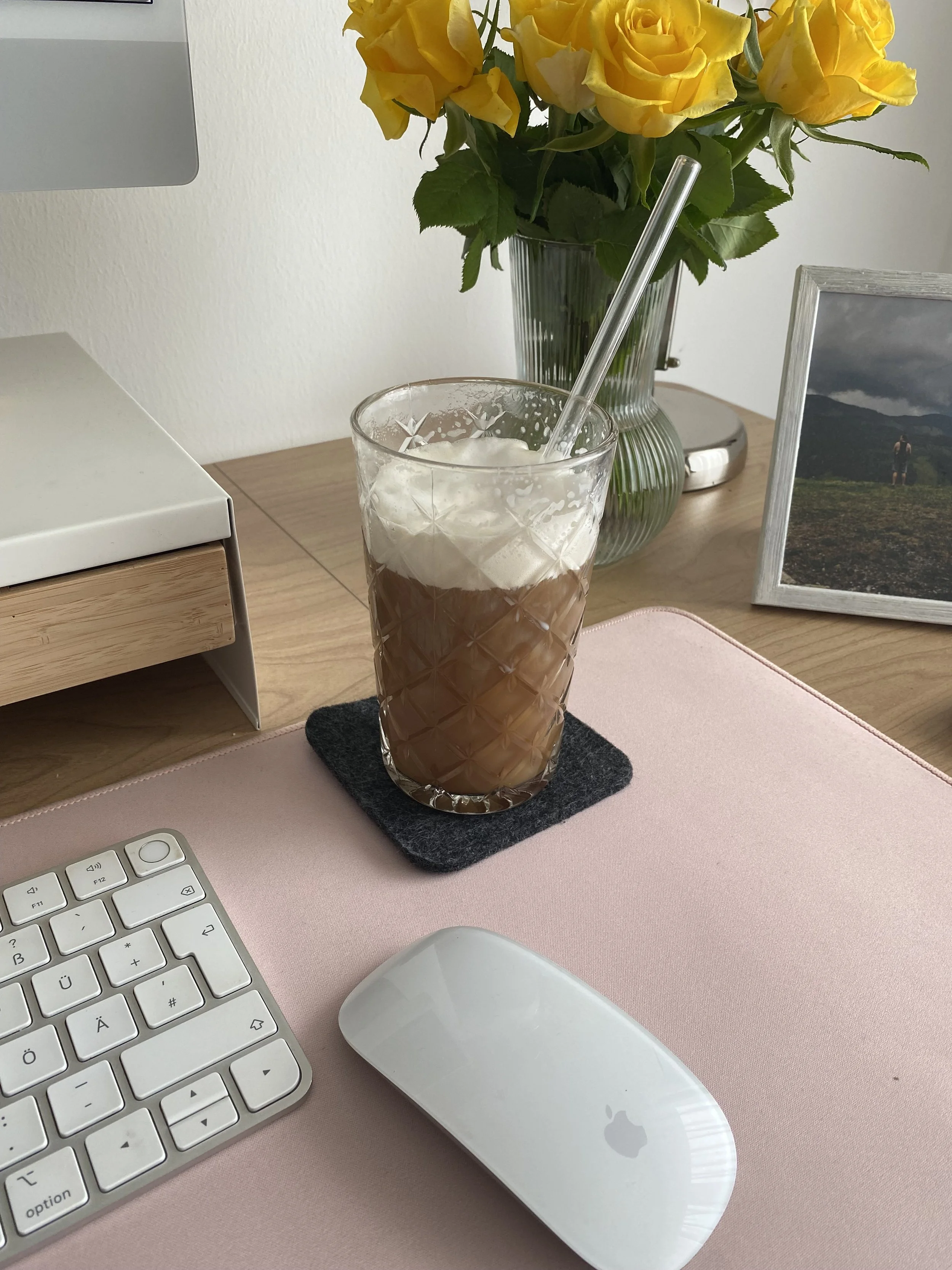 Eiskaffee steht vor einem Strauß gelber Rosen auf einem Schreibtisch.