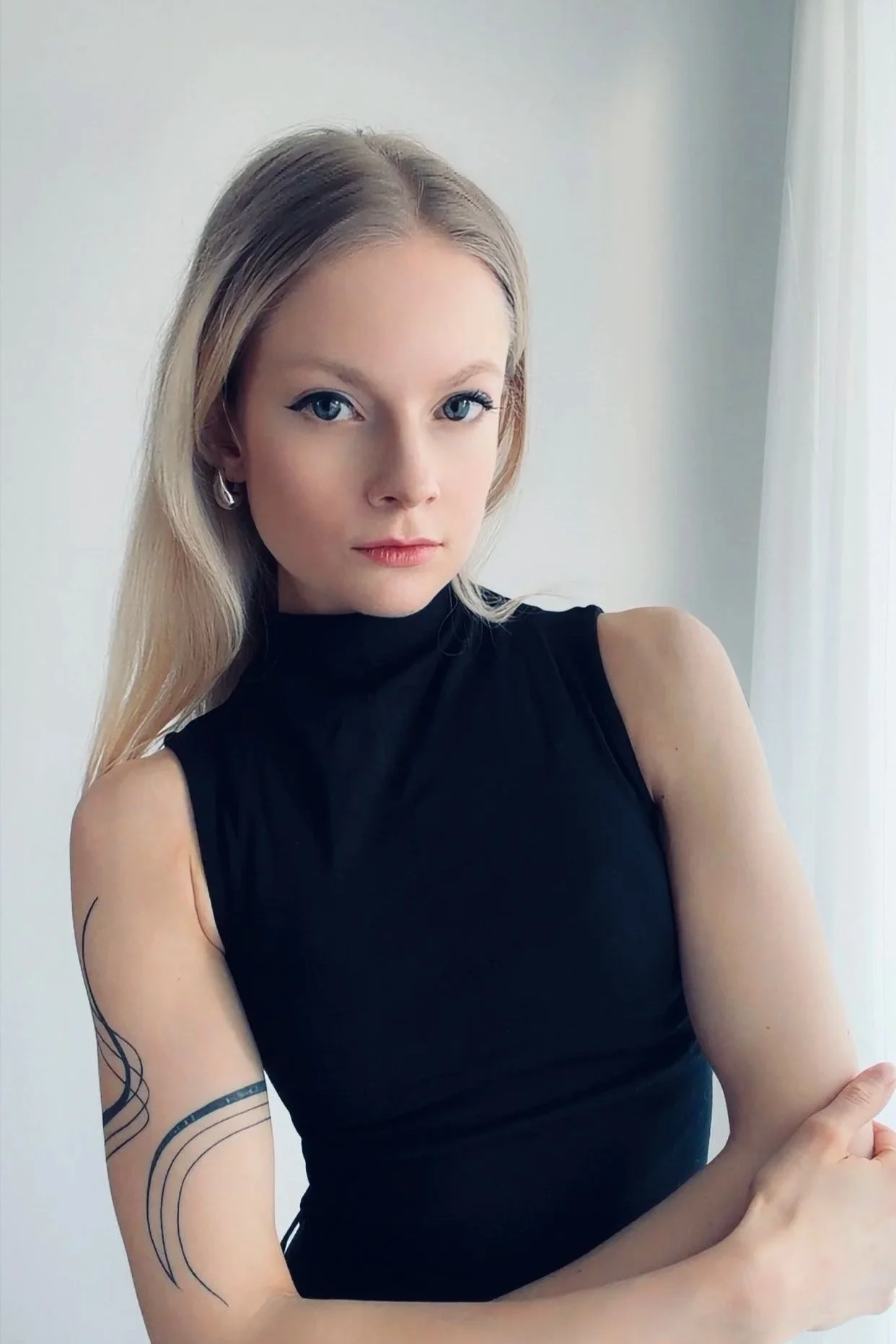 Blonde Frau mit schwarzem ärmellosen Oberteil blickt in die Kamera.