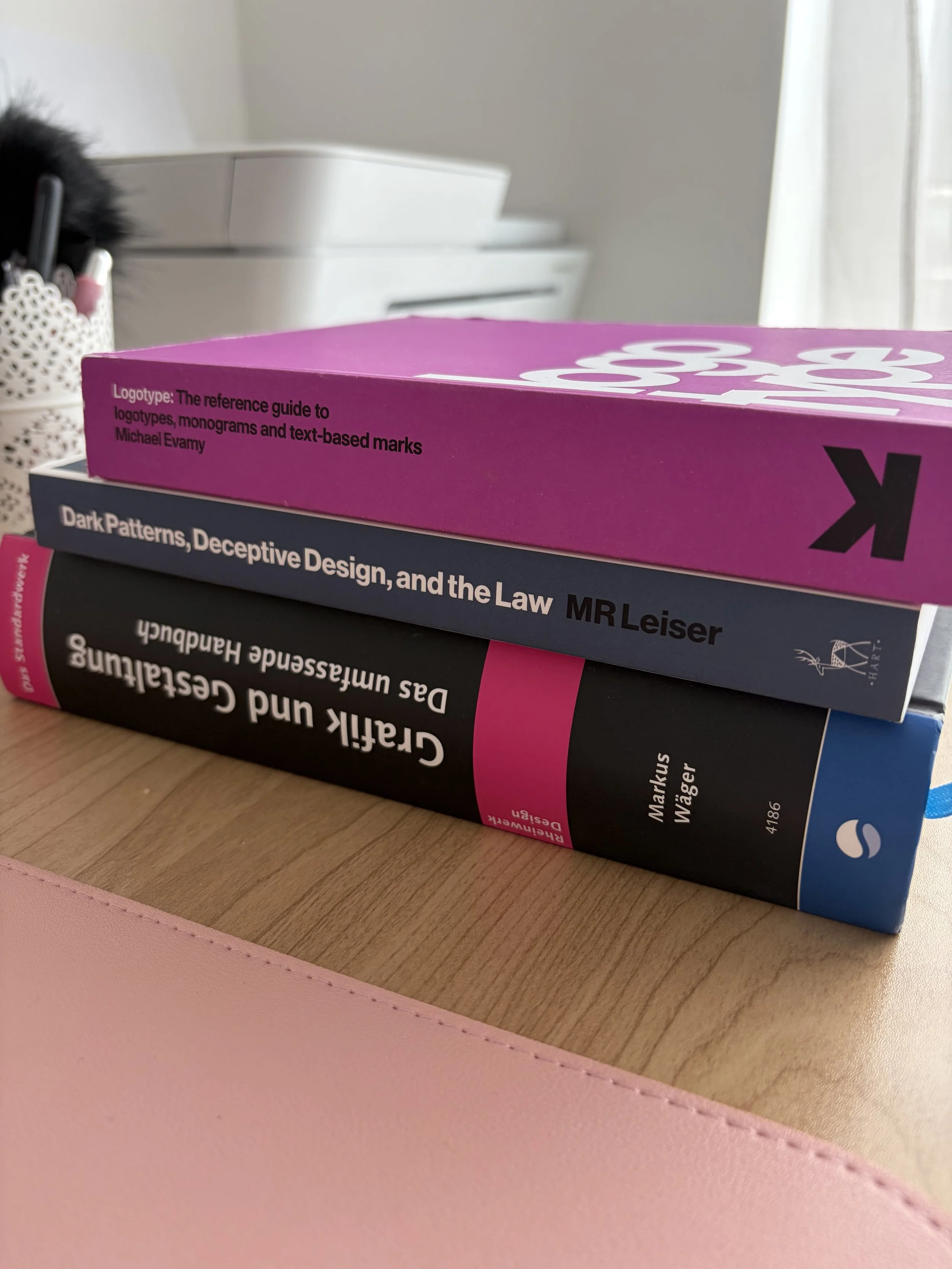 Drei Bücher liegen gestapelt auf einem Schreibtisch.