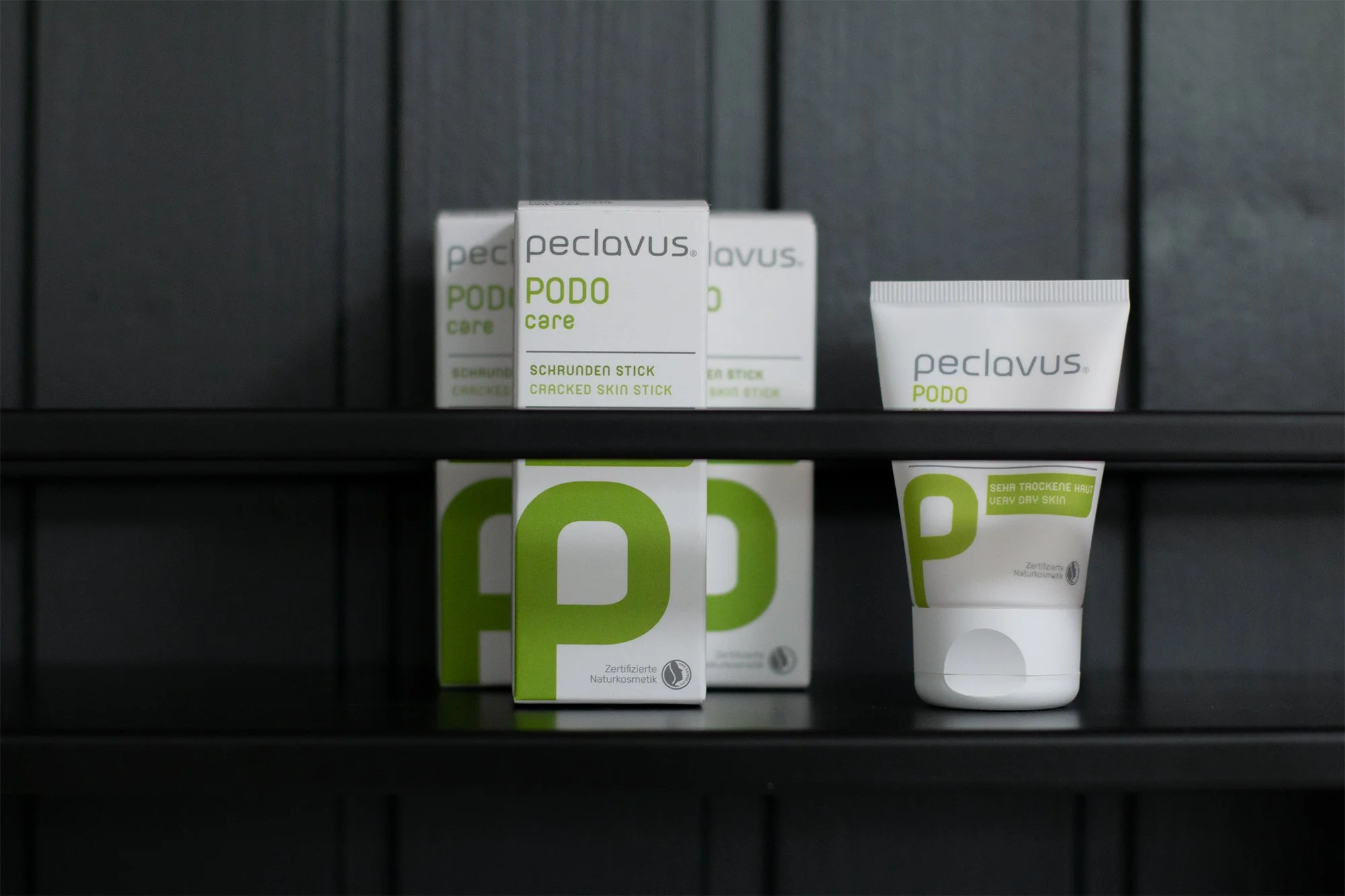 Verpackungen von Peclavus Podo Care Produkten auf einem schwarzen Regal.