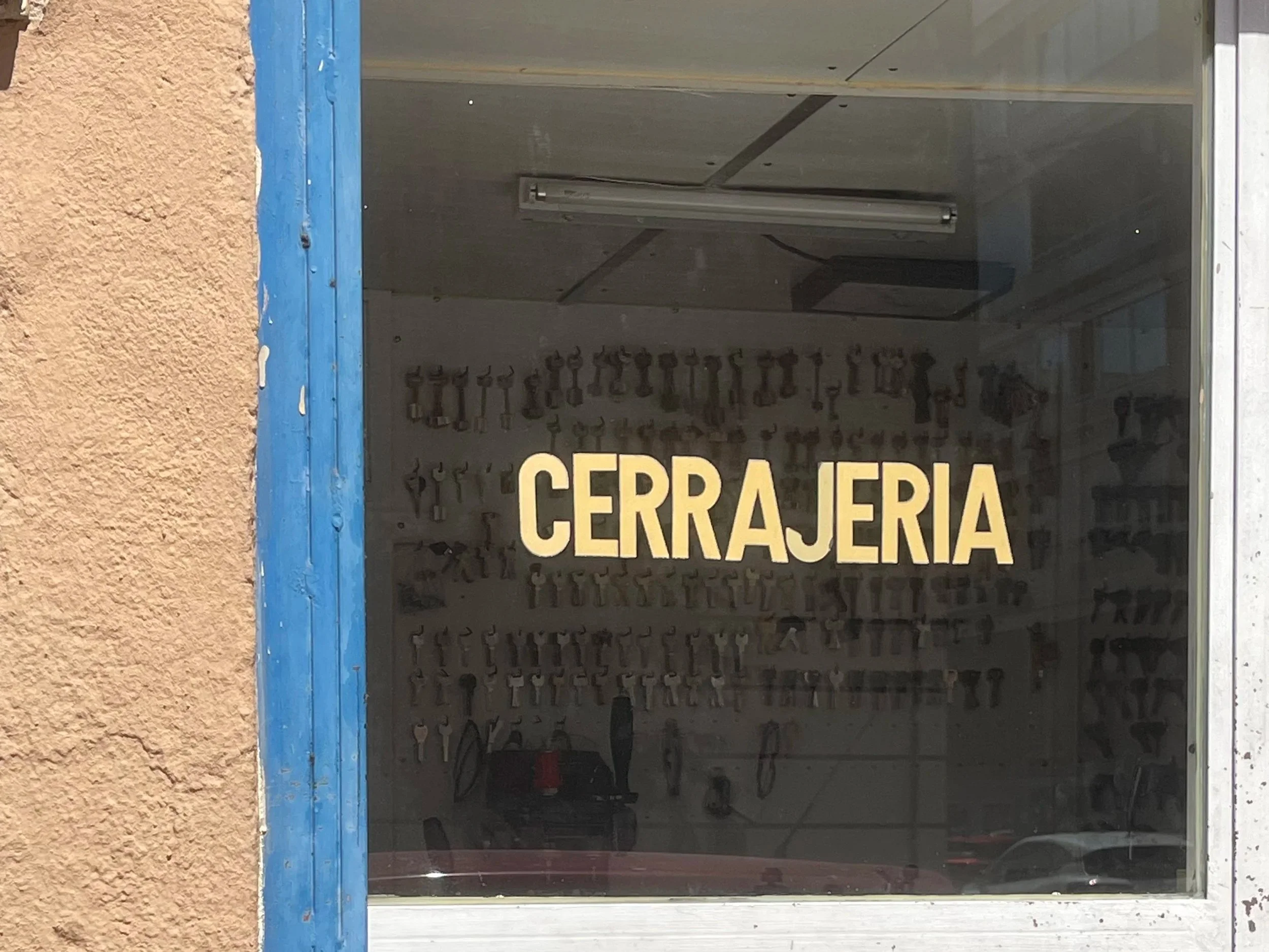 Ventana con cartel que dice 'CERRAJERÍA' y herraduras colgadas en la parte trasera.