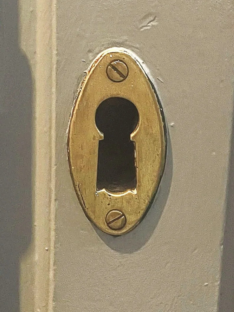 Imagen de una cerradura de ojo de cerradura en una puerta metálica con tornillos visibles.