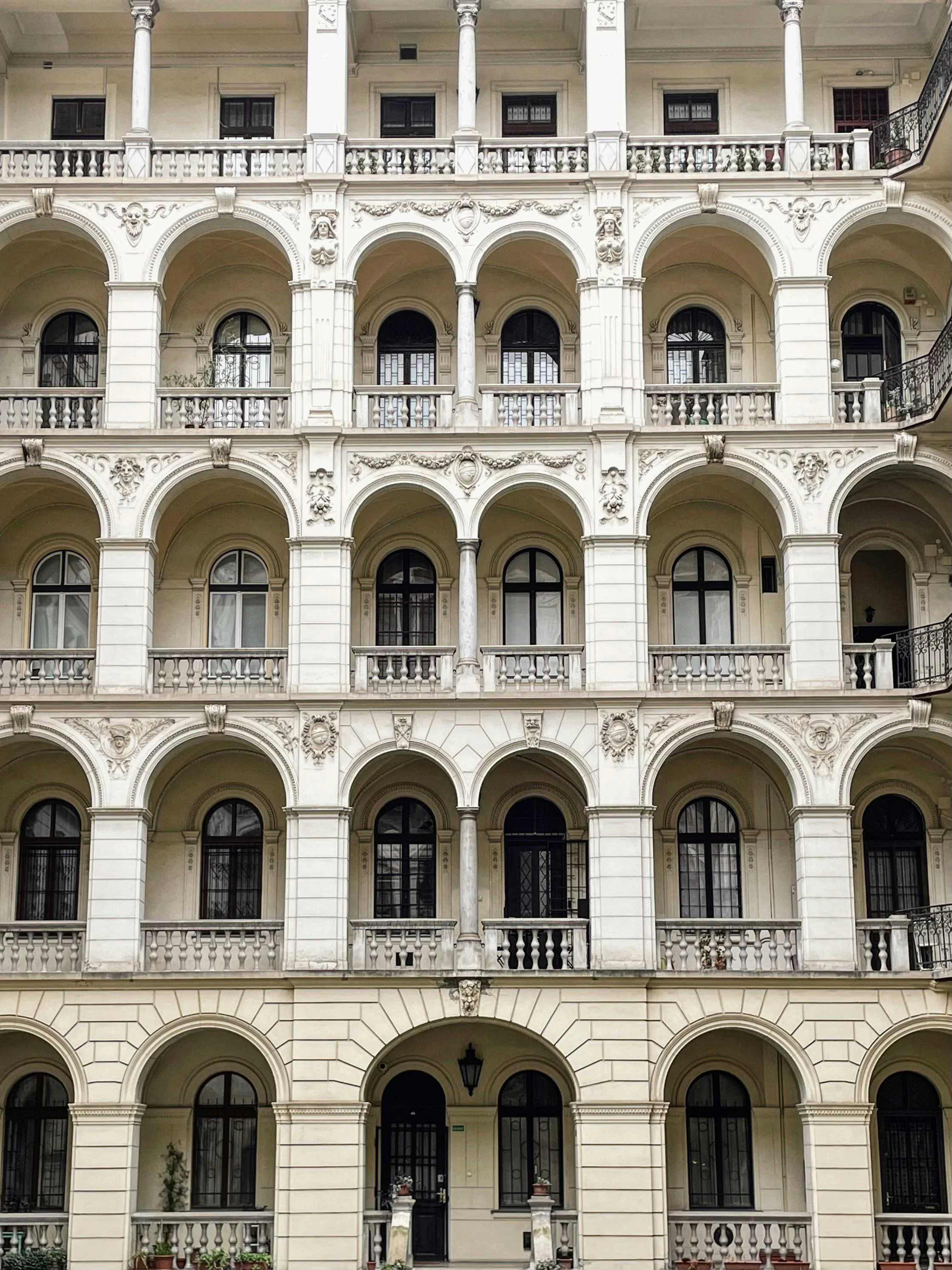 Front view of a multi-story building with classical architectural elements including arched windows and balconies. The building features detailed sculptural decorations, columns, and balustrades.