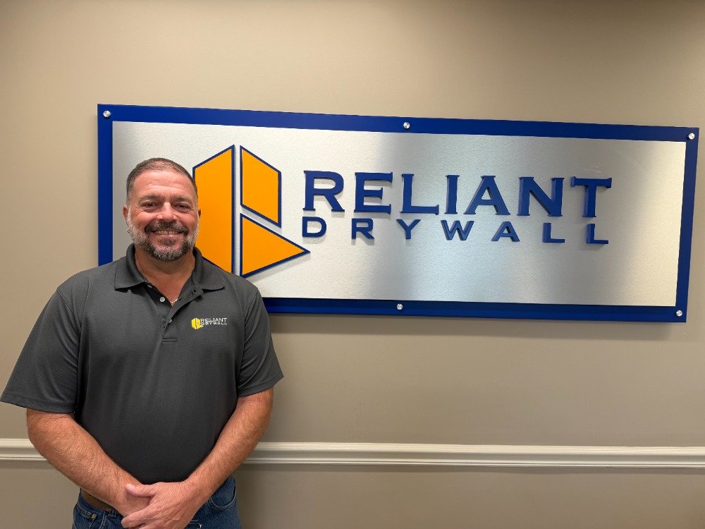 Man standing in front of Reliant Drywall company sign on a wall