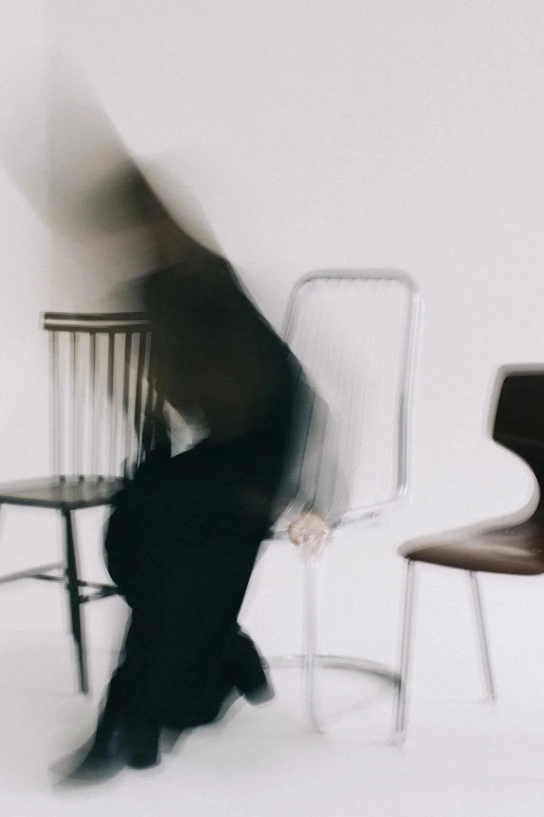 Eine Person sitzt auf einem Stuhl vor einer weißen Wand, während sie sich nach vorne beugt. Der Kopf und die Arme sind in Bewegung.