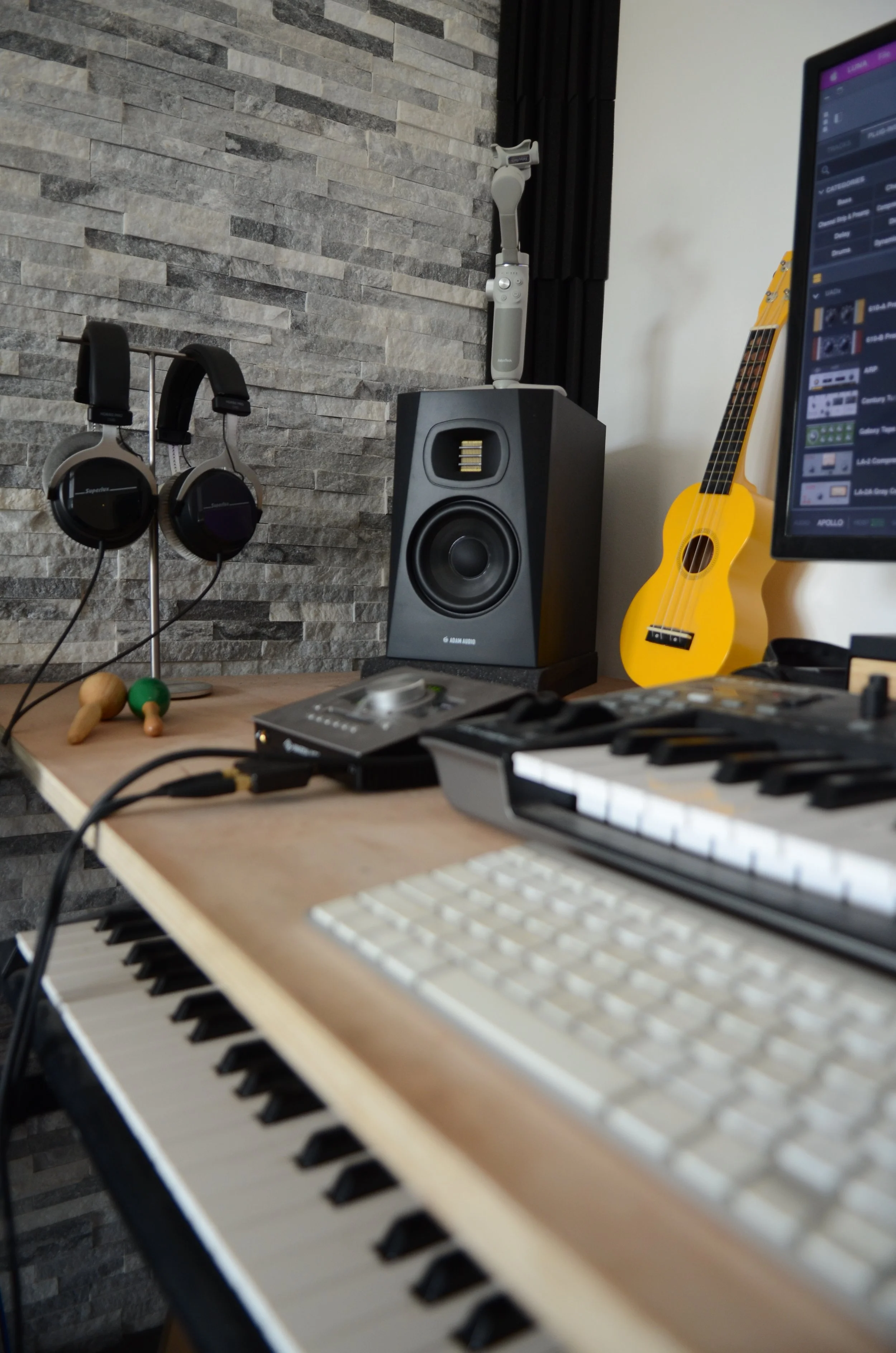 Un espace de musique contenant un clavier, un ordinateur portable, une paire de haut-parleurs, un micrologiciel, une guitare jaune, un microphone, des écouteurs, une souris et un écran d'ordinateur.