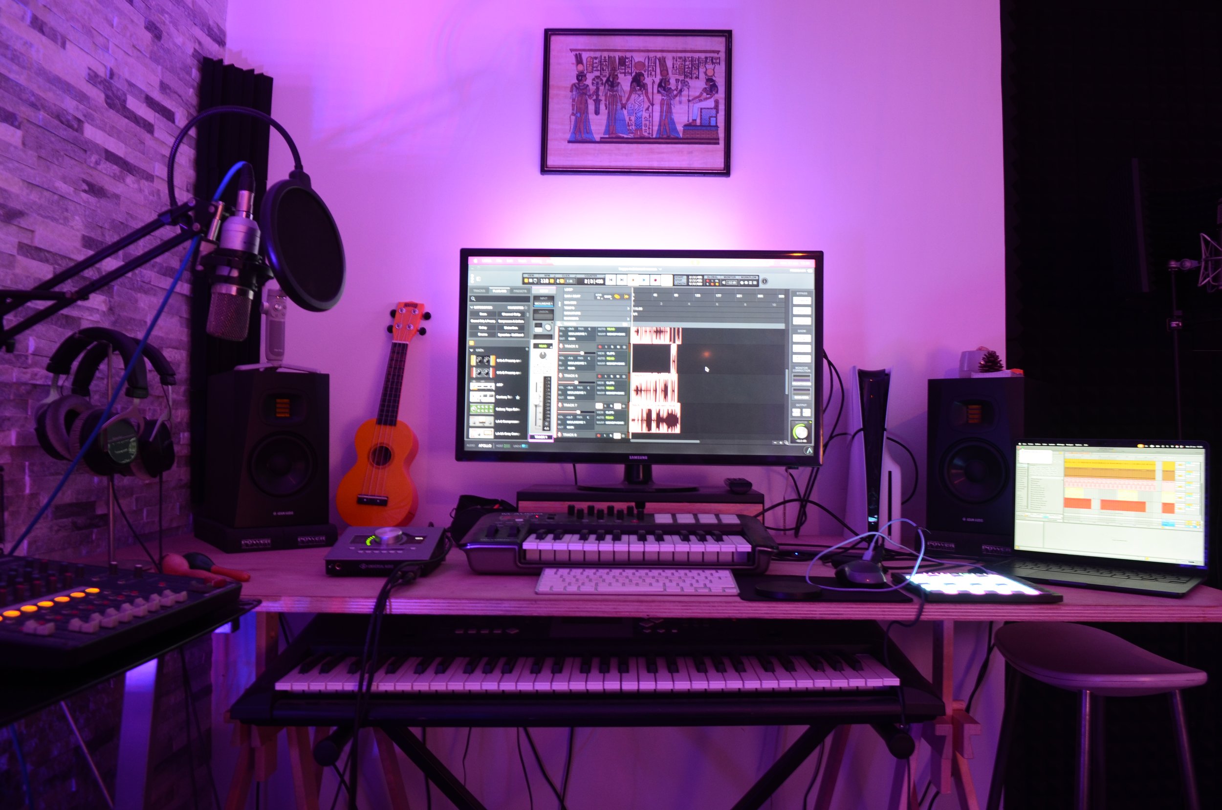 Un studio de musique avec un ordinateur affichant un logiciel de création musicale, un clavier, une guitare, un microphone, une paire de haut-parleurs, des écouteurs, et un tableau de lights violet et rose