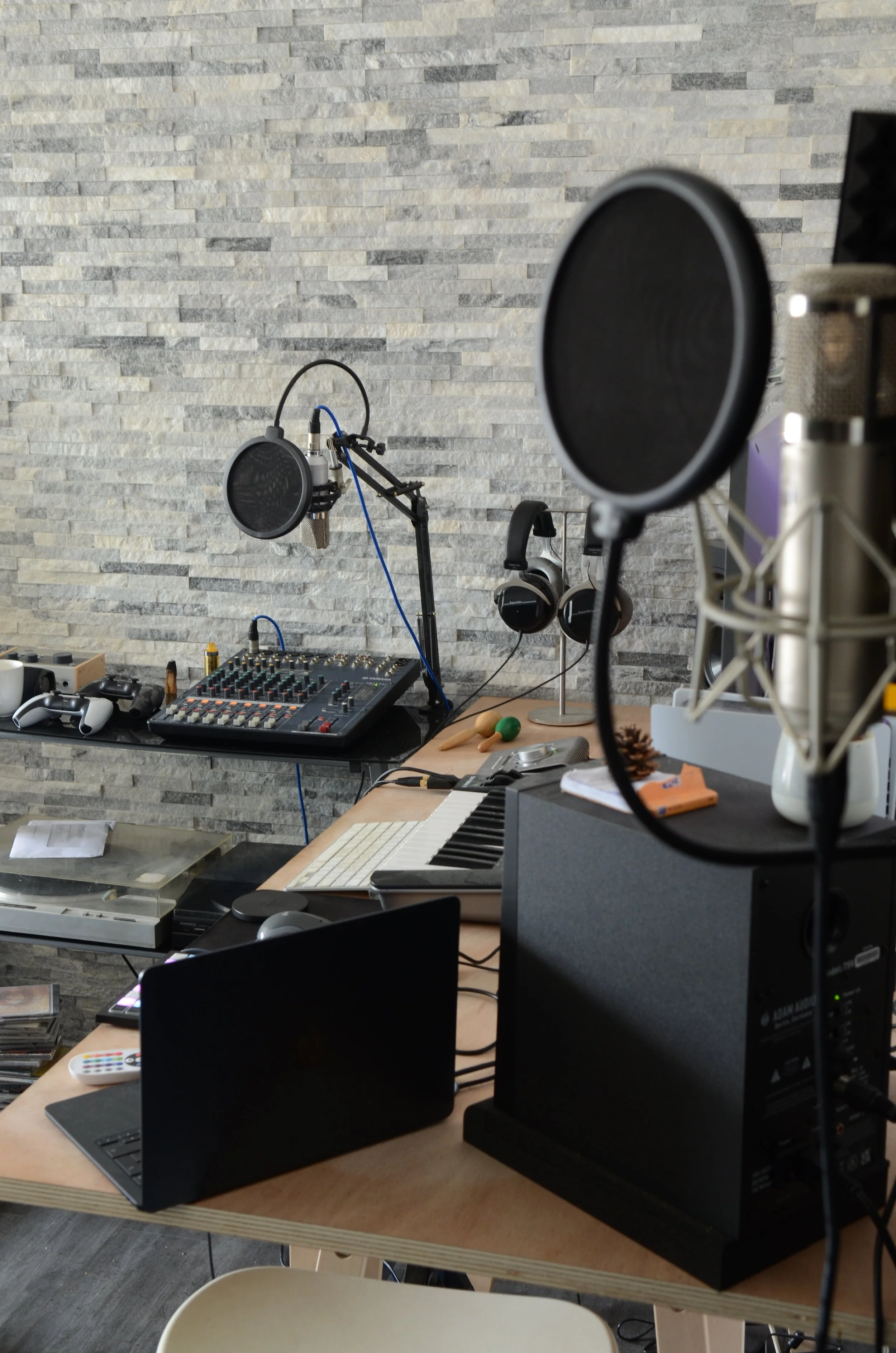 Studio d'enregistrement avec microphones, casque audio, console de mixage, ordinateur portable, clavier, haut-parleur et divers équipements musicaux sur une table en bois.