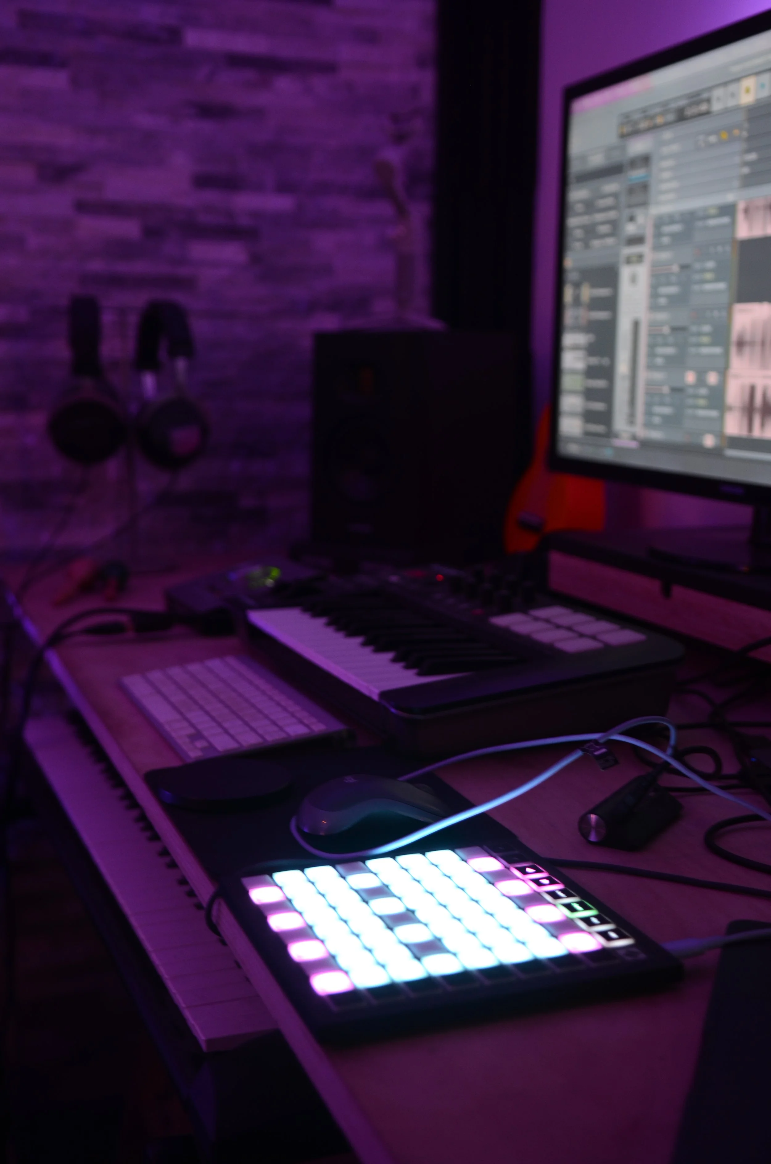 Salle de musique électronique avec clavier, contrôleur MIDI lumineux, ordinateur avec interface audio, casque audio noir accroché à un mur en briques, éclairage violet espacé.