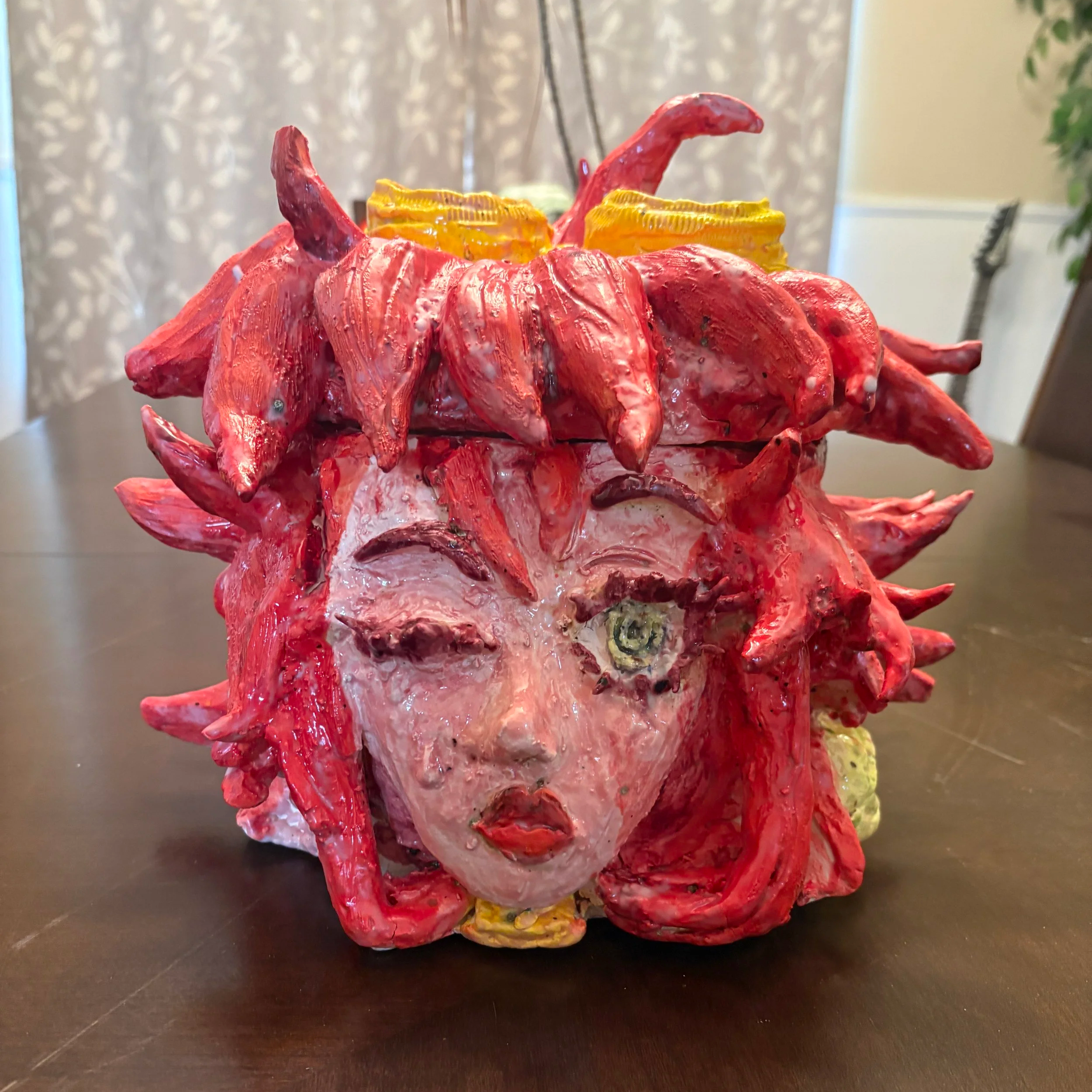 A decorative sculpture resembling a cat with prominent ears, painted in red and yellow, with a shiny surface, placed on a dark table indoors.